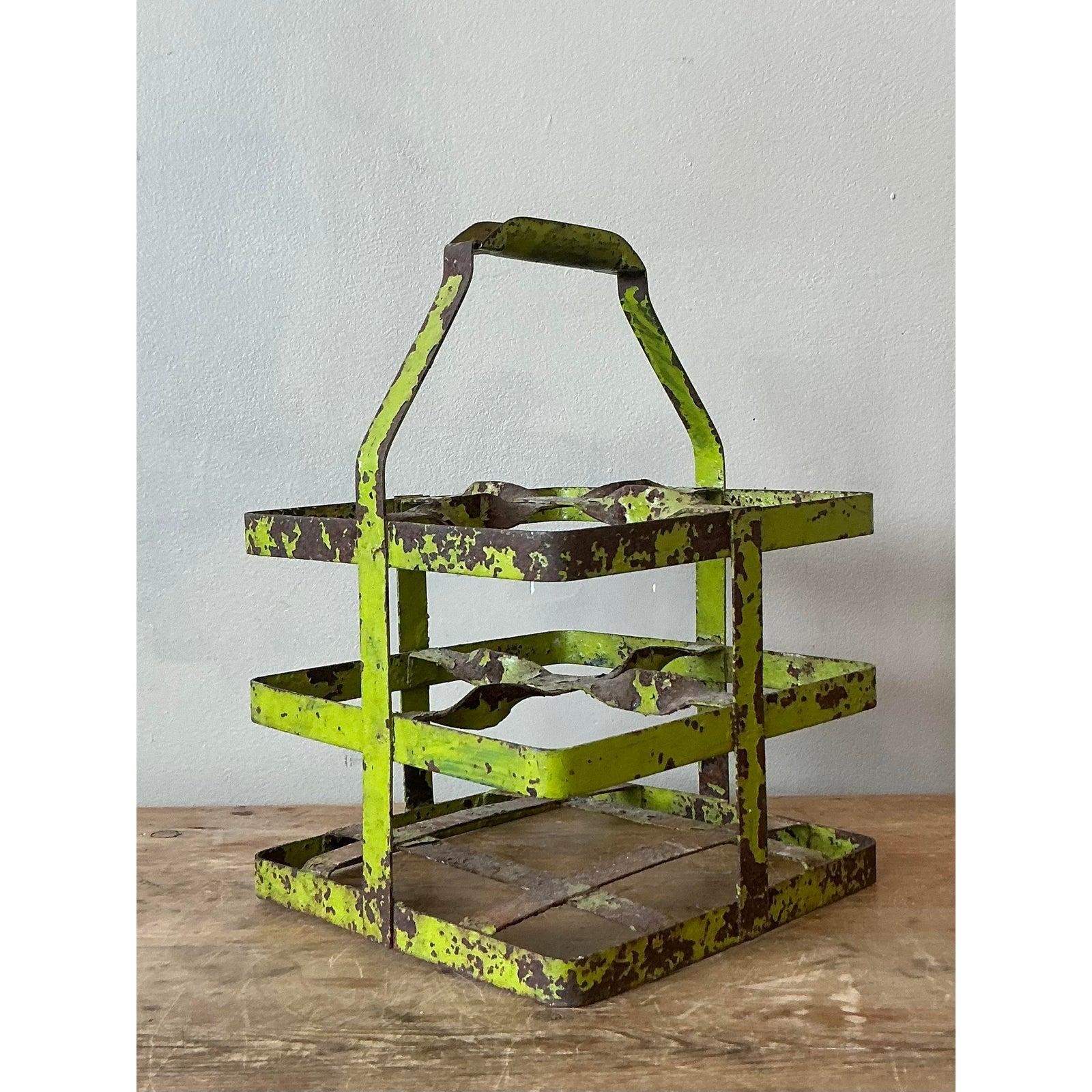 Embrace the raw charm and utilitarian appeal of this vintage Boho distressed bottle carrier. Crafted from sturdy metal and finished in a vibrant, aged green, this piece exudes an authentic industrial character that is both functional and decorative.