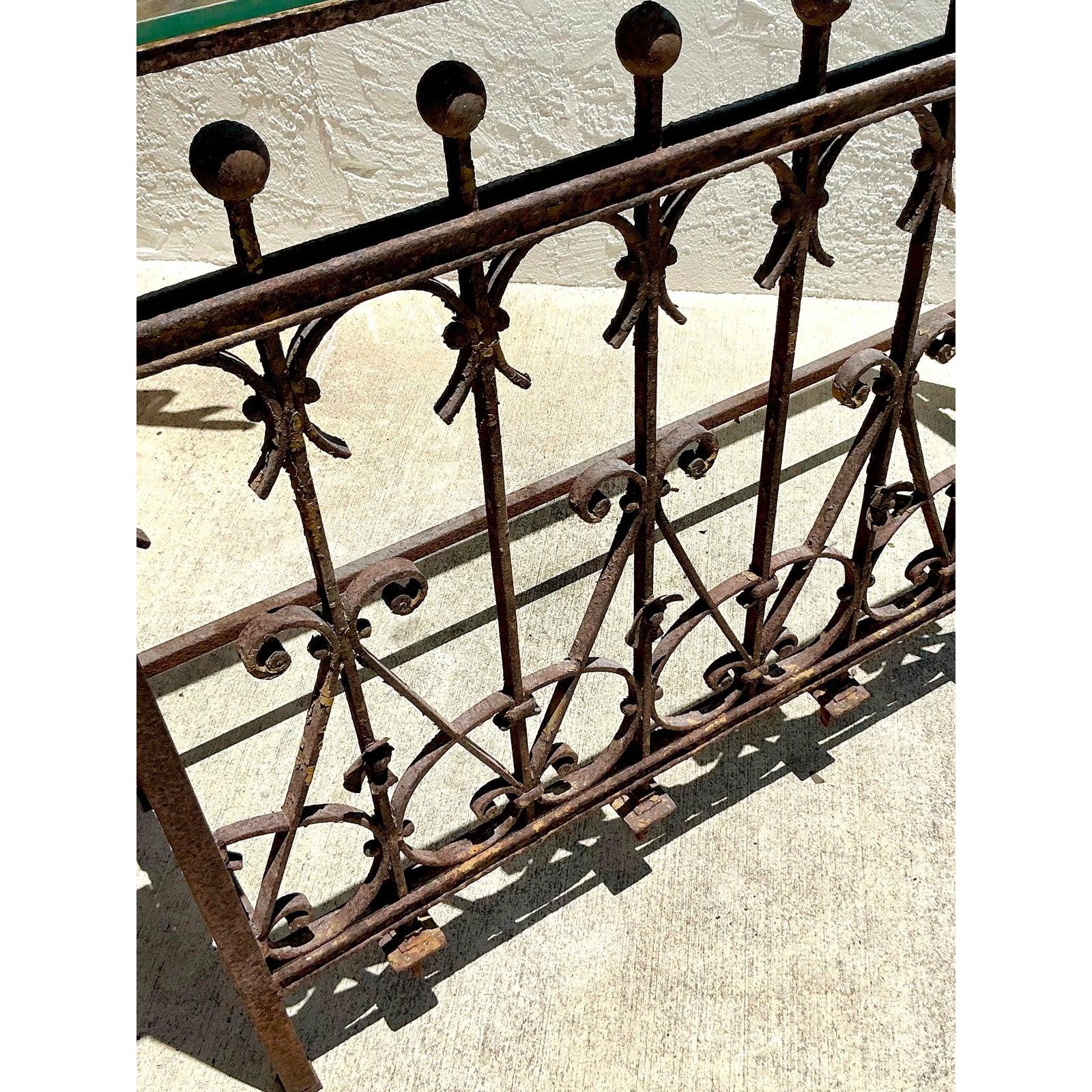 Evoke a sense of timeless romance and artisanal charm with this captivating Vintage Distressed Wrought Iron Console Table, complete with its original glass top. Hand-forged with intricate scrollwork, delicate spindles, and striking pointed finials