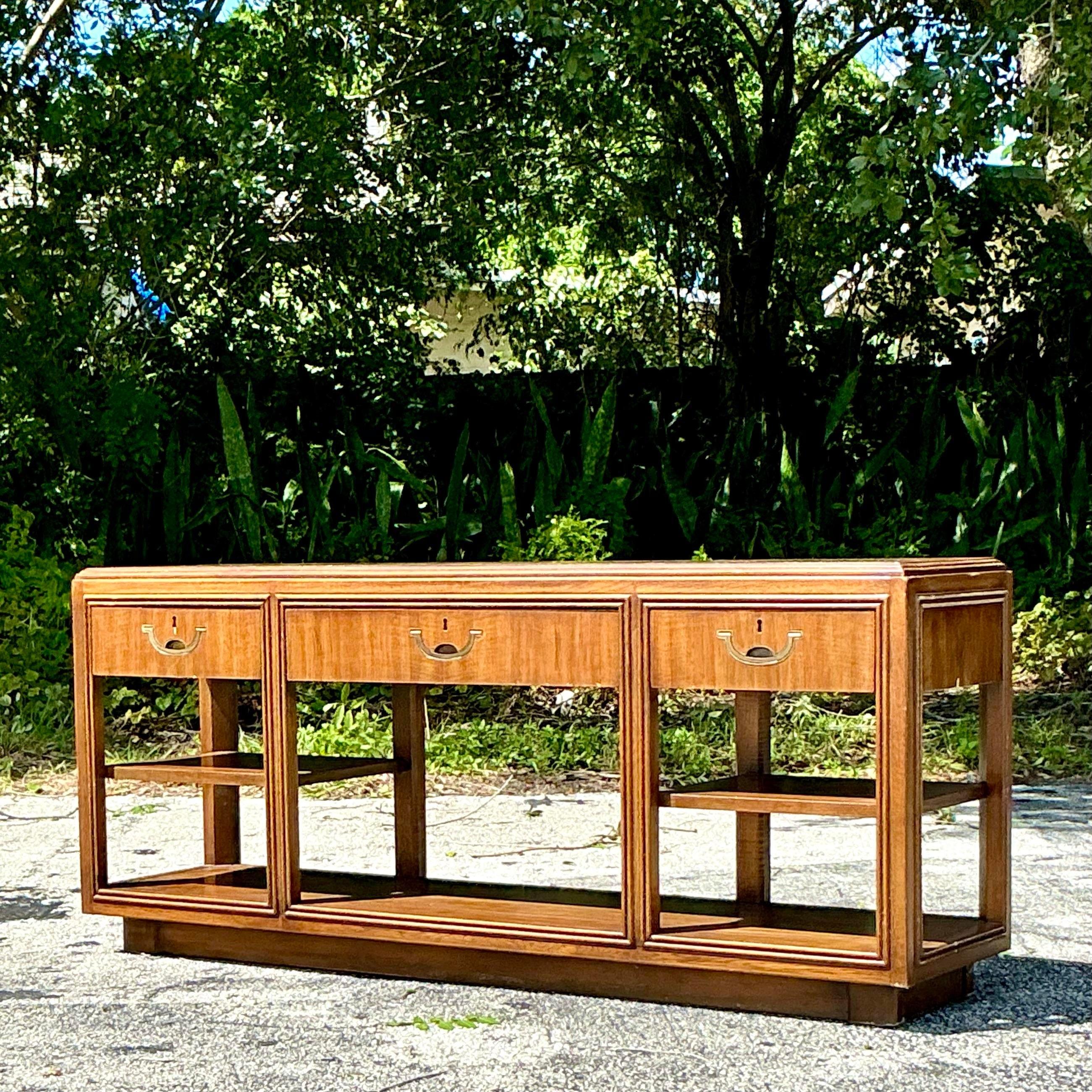 This Vintage Boho Drexel Heritage Campaign Console Table blends bohemian flair with classic campaign style. Crafted with sleek lines and brass accents, it offers versatile storage and timeless charm, perfect for an entryway or living room