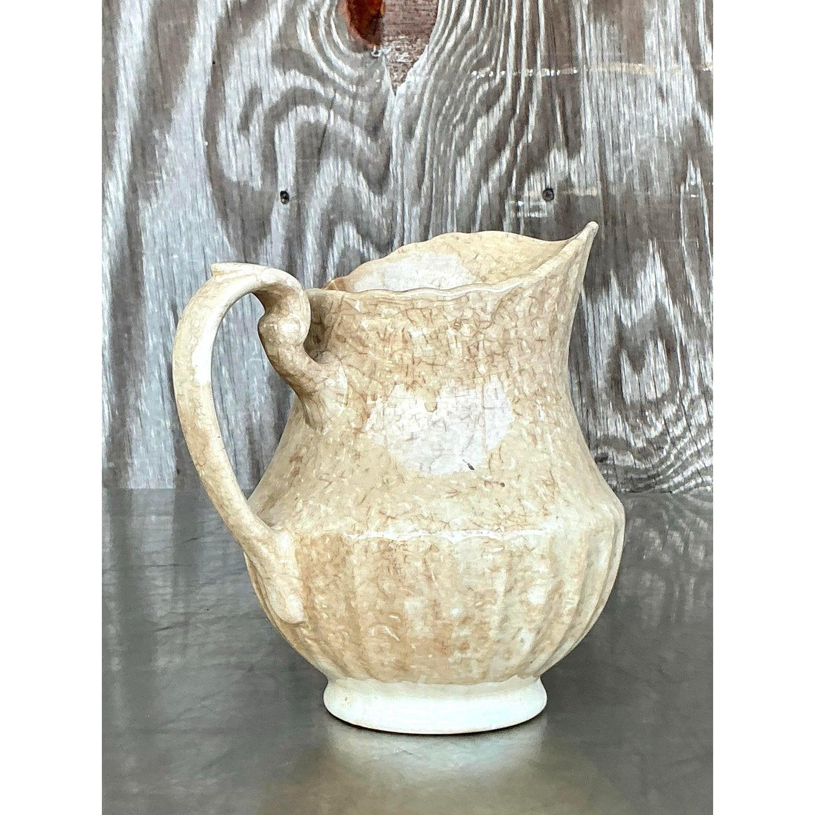 Infuse rustic charm into your interior with this Vintage Boho Eakin Stoneware Pitcher, a beautifully aged vessel rich in texture and character. Featuring an organically rippled rim, scalloped base, and a gracefully curved handle, this ceramic