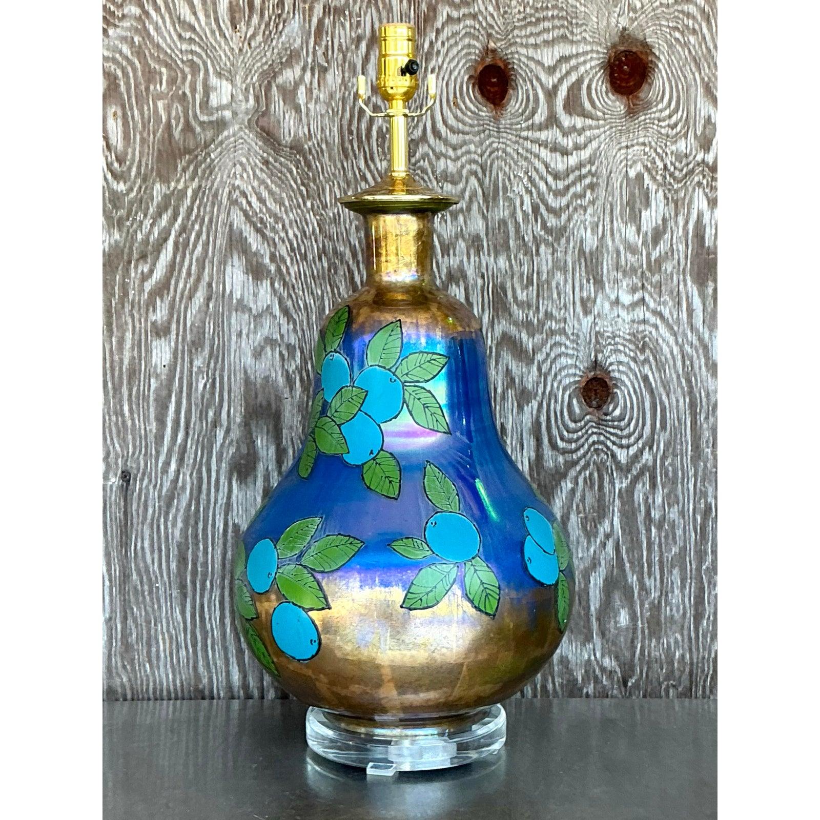 This stunning vintage églomisé table lamp exudes bohemian charm with its captivating hand-painted design and iridescent gold and blue glass finish. The graceful pear-shaped form is adorned with delicate foliage and fruit motifs, creating a striking