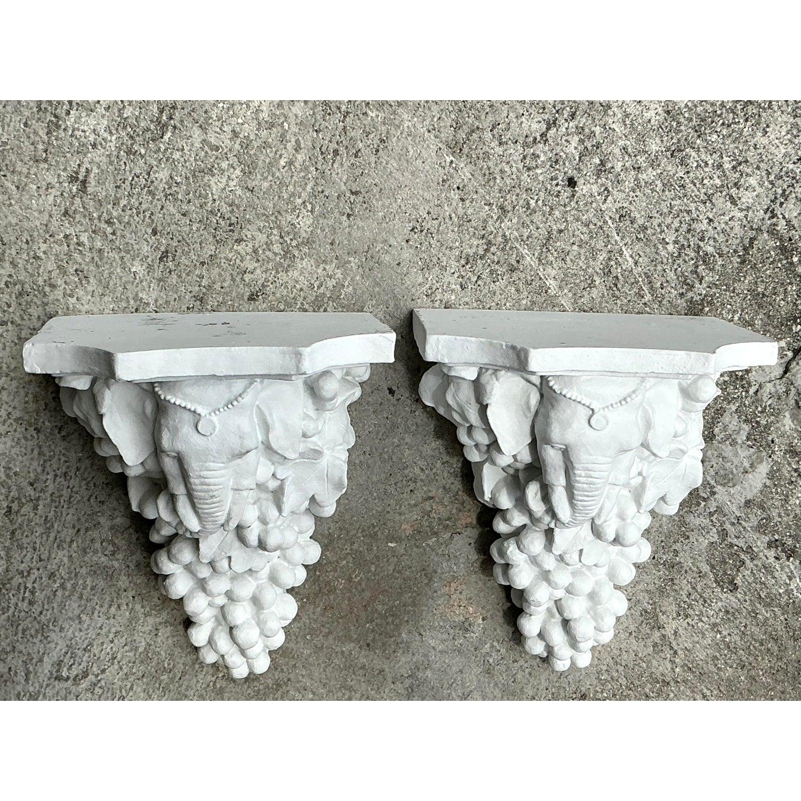 Verleihen Sie Ihrem Raum einen kühnen, eklektischen Touch mit diesem auffälligen Paar Vintage Boho Elephant Brackets. Fachmännisch in einer klassischen Kragstein-Silhouette geformt, zeigt jede Konsole einen kunstvoll geschnitzten Elefantenkopf mit