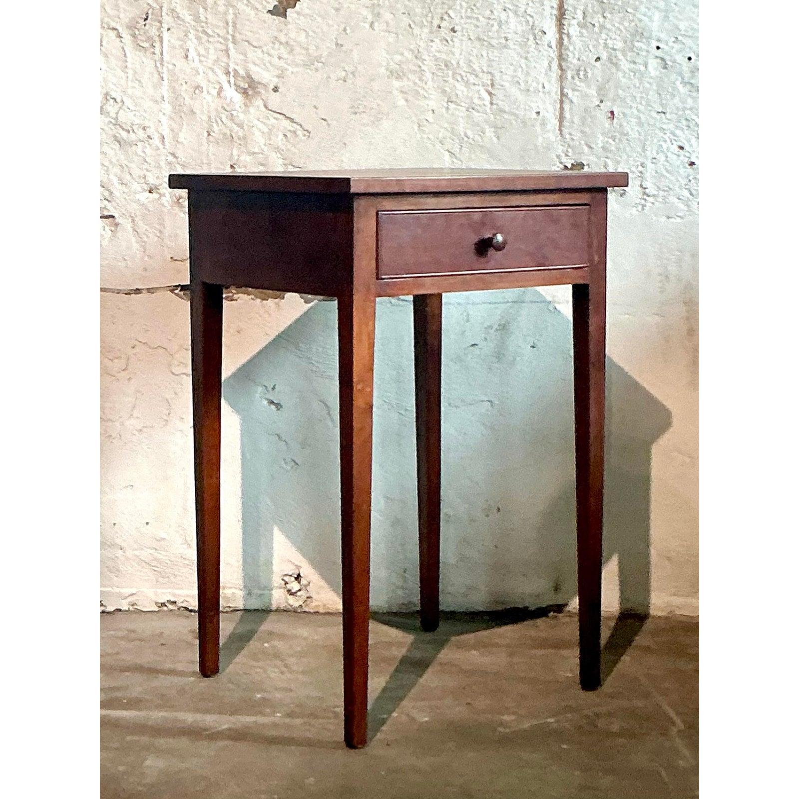 Unearth a piece of enduring American craftsmanship with this elegant Vintage Federal Style Accent Table. Characterized by its clean lines and minimalist silhouette, this charming table features slender, tapered legs and a single, functional drawer