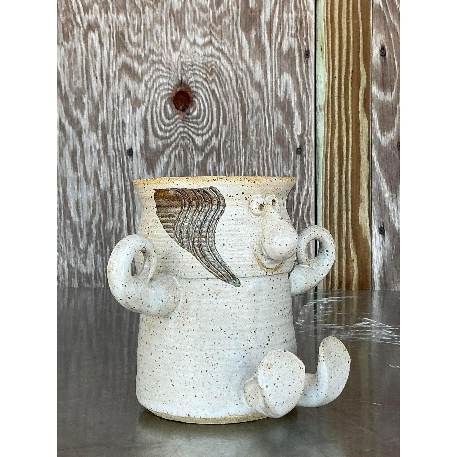 Unleash a dose of playful charm with this truly unique vintage studio pottery vase. A delightful testament to artisan craftsmanship, this piece takes on an endearing figurative form, complete with a whimsical face, expressive 