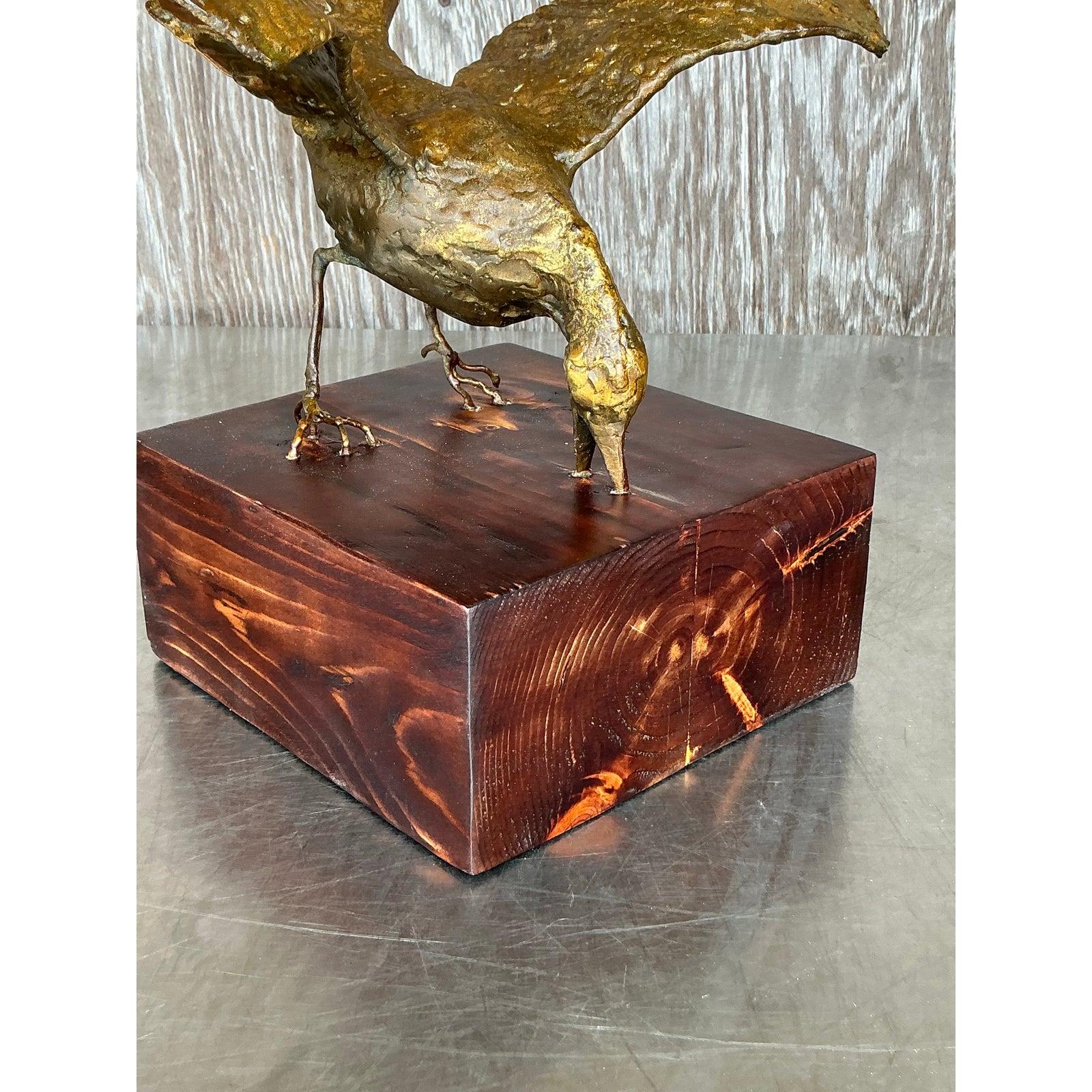 À la fois gracieuse et imposante, cette sculpture d'oiseau vintage dorée capture l'instant du vol avec un mouvement et une texture saisissants. Réalisée dans une posture dramatique avec des ailes déployées, cette pièce repose sur une base en bois