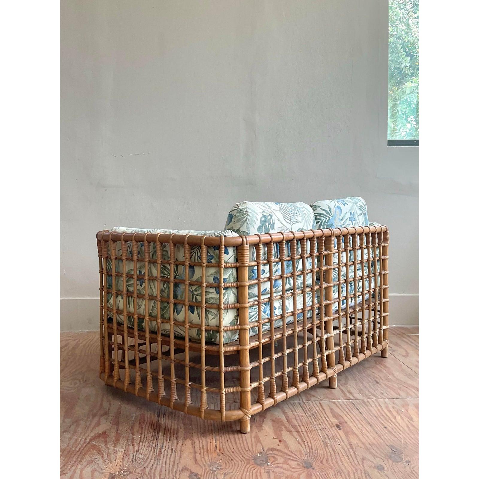 A stunning vintage loveseat that channels the iconic and highly sought-after designs of Henry Olko for McGuire. This piece is a masterwork of organic modernism, featuring a substantial rattan frame with beautiful faux bamboo detailing and classic