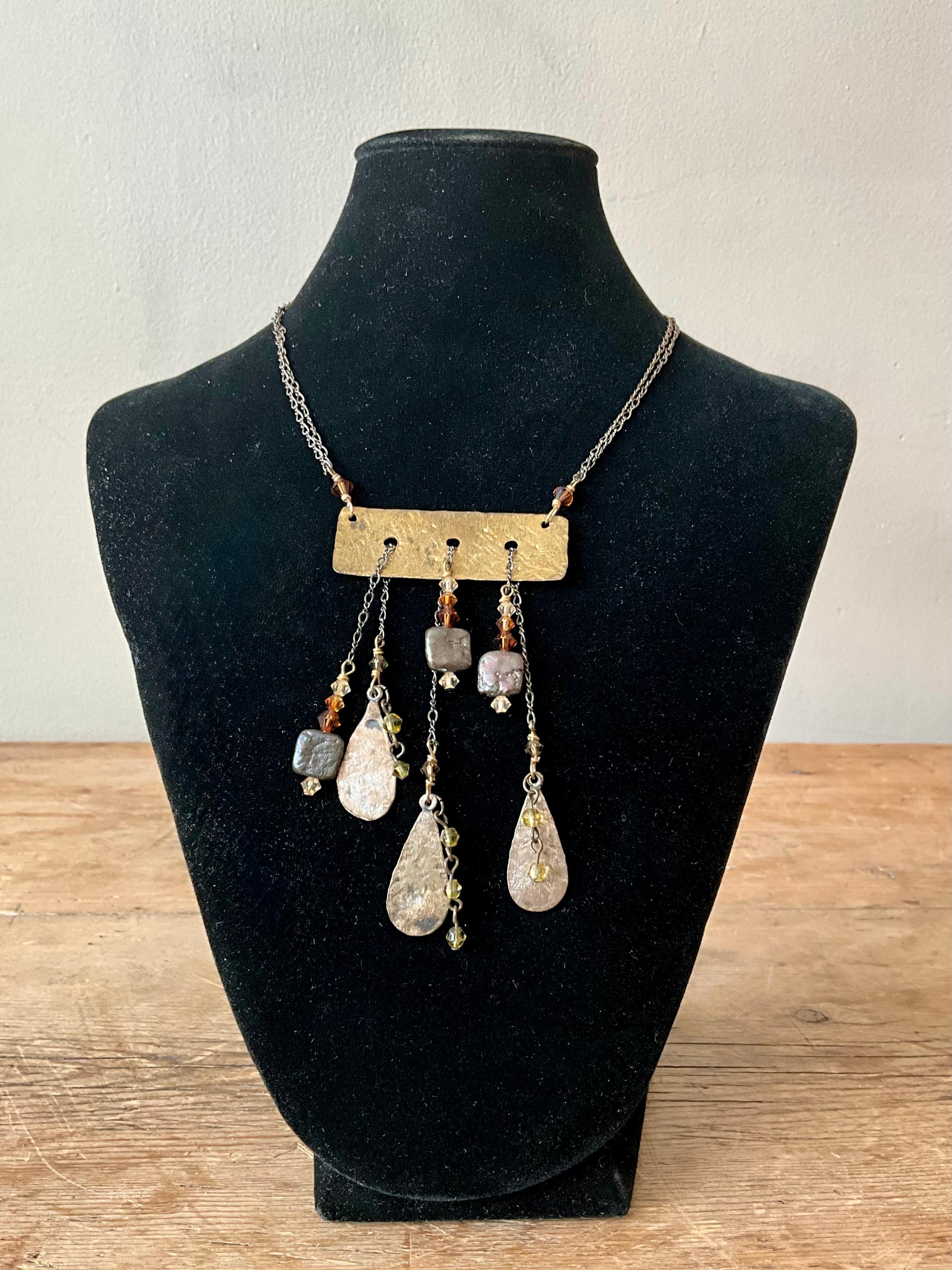 This vintage Boho hammered brass drop necklace exudes earthy elegance and free-spirited charm. Featuring a series of organically shaped, hand-hammered brass elements, it showcases warm golden tones with a rustic, artisan finish. The textured surface