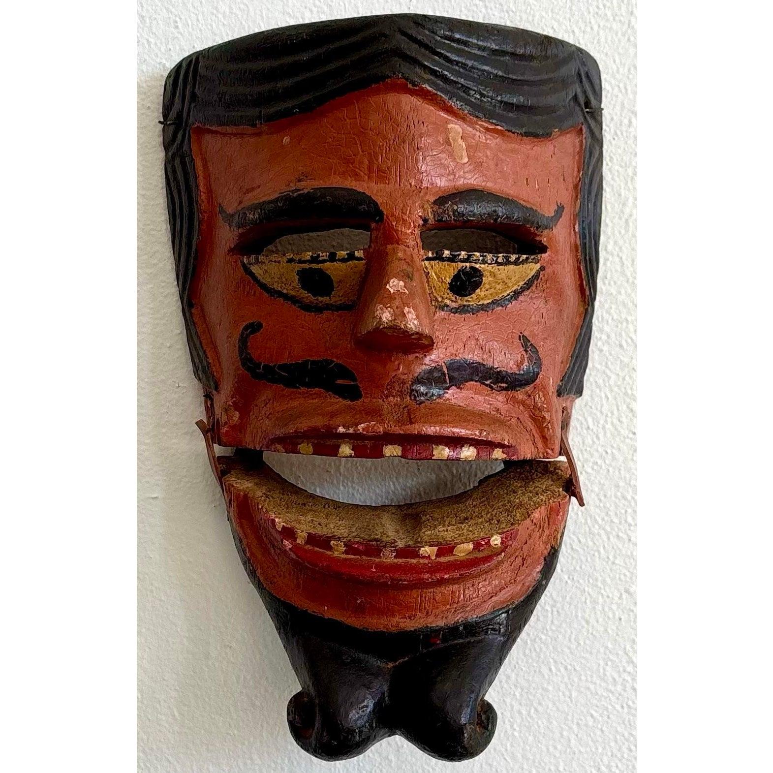 Questa espressiva maschera in legno intagliato è piena di personalità e di fascino teatrale. Con le sue sopracciglia audaci, i baffi arricciati e la mascella ben definita, sembra incarnare un personaggio malizioso o cattivo, forse proveniente dal