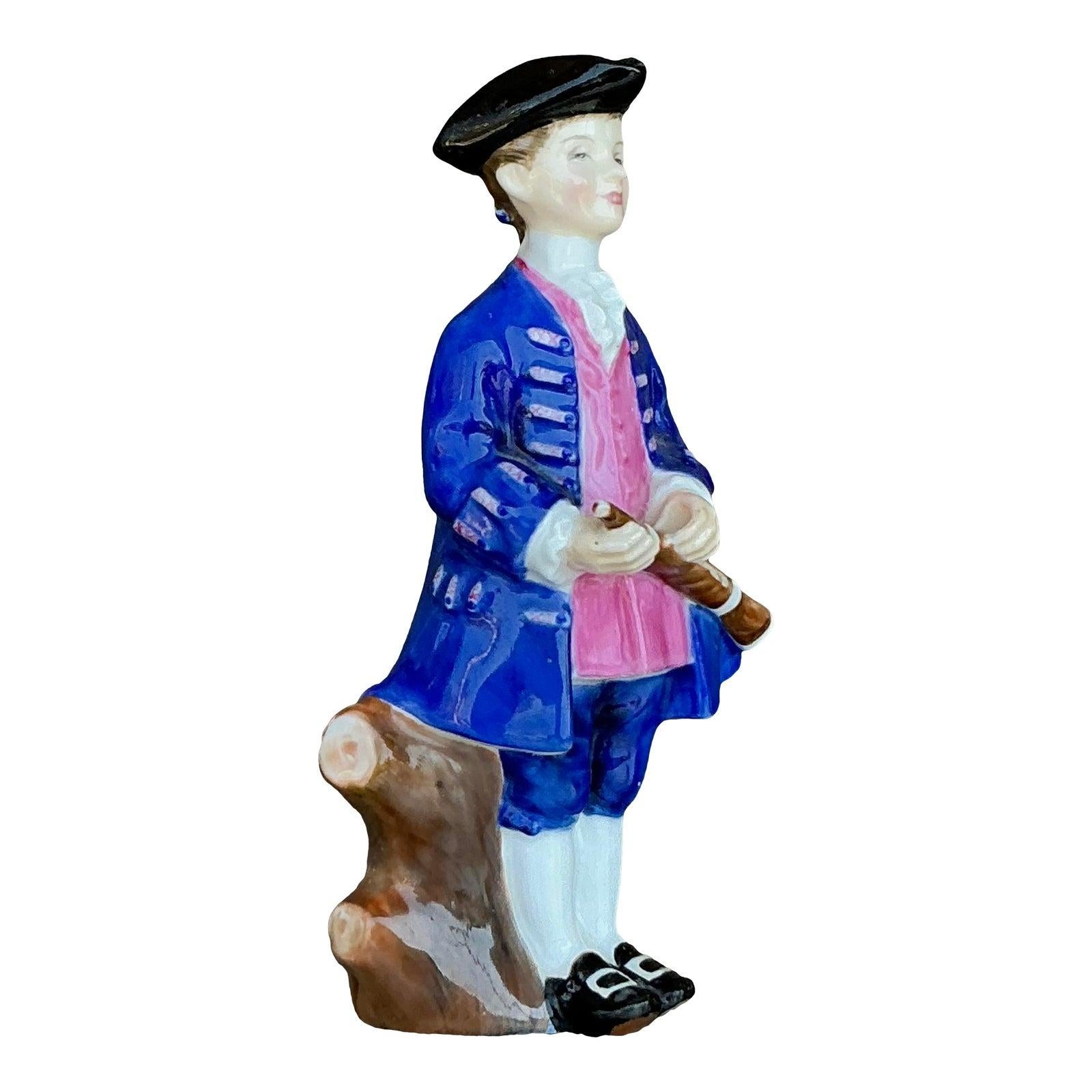 Dai un tocco di raffinato estro e fascino storico al tuo arredamento con questa figura militare in ceramica vintage dipinta a mano. Vestita con un cappello a tricorno in stile XVIII secolo e un cappotto regale blu e rosa, questa statuetta tiene in