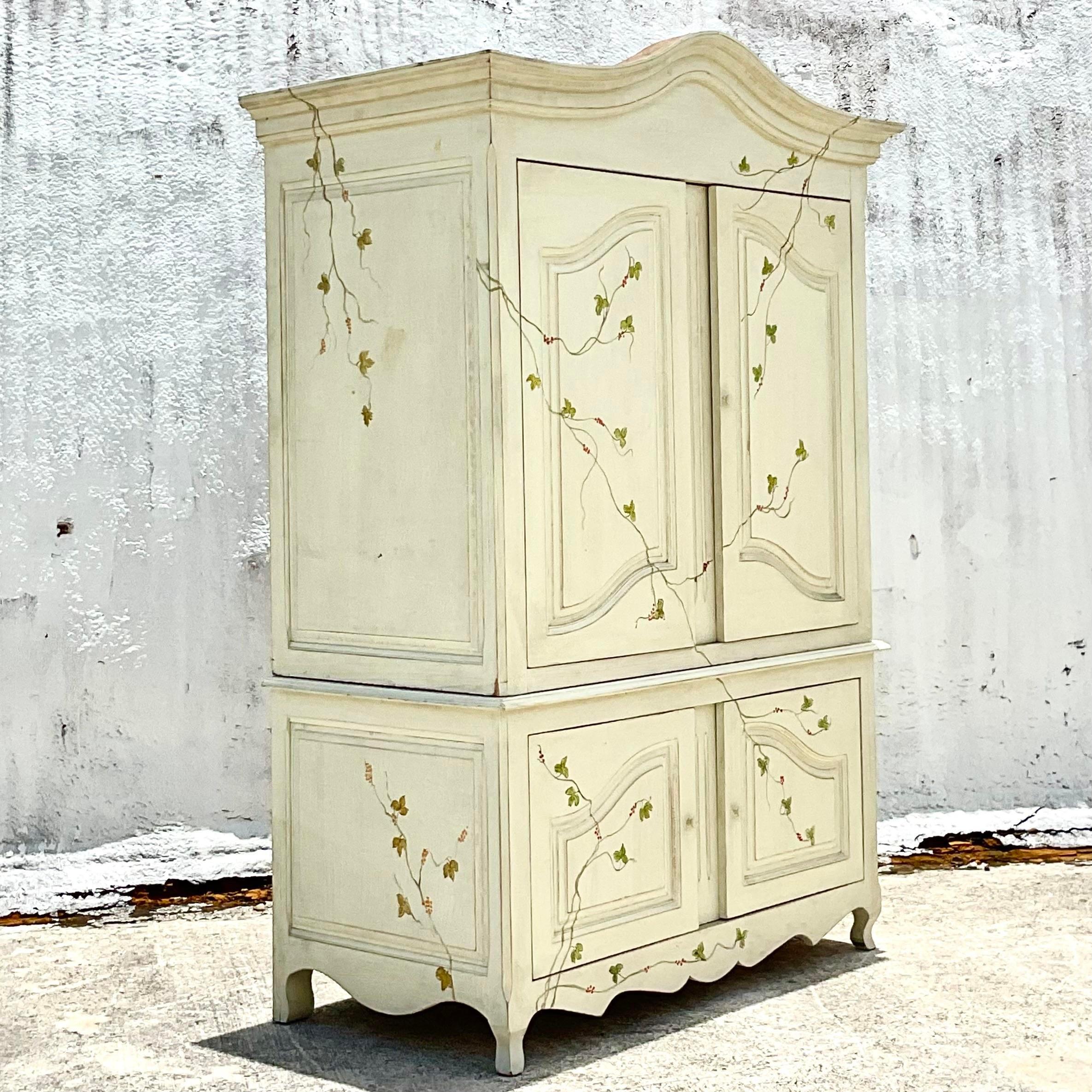 Fantastic vintage monumental armoire. A beautiful hand painted vine on a white background. Currently outfitted as a media cabinet, but would be beautiful converted to a dry bar or just add a hang bar for extra storage. Acquired from a Palm Beach