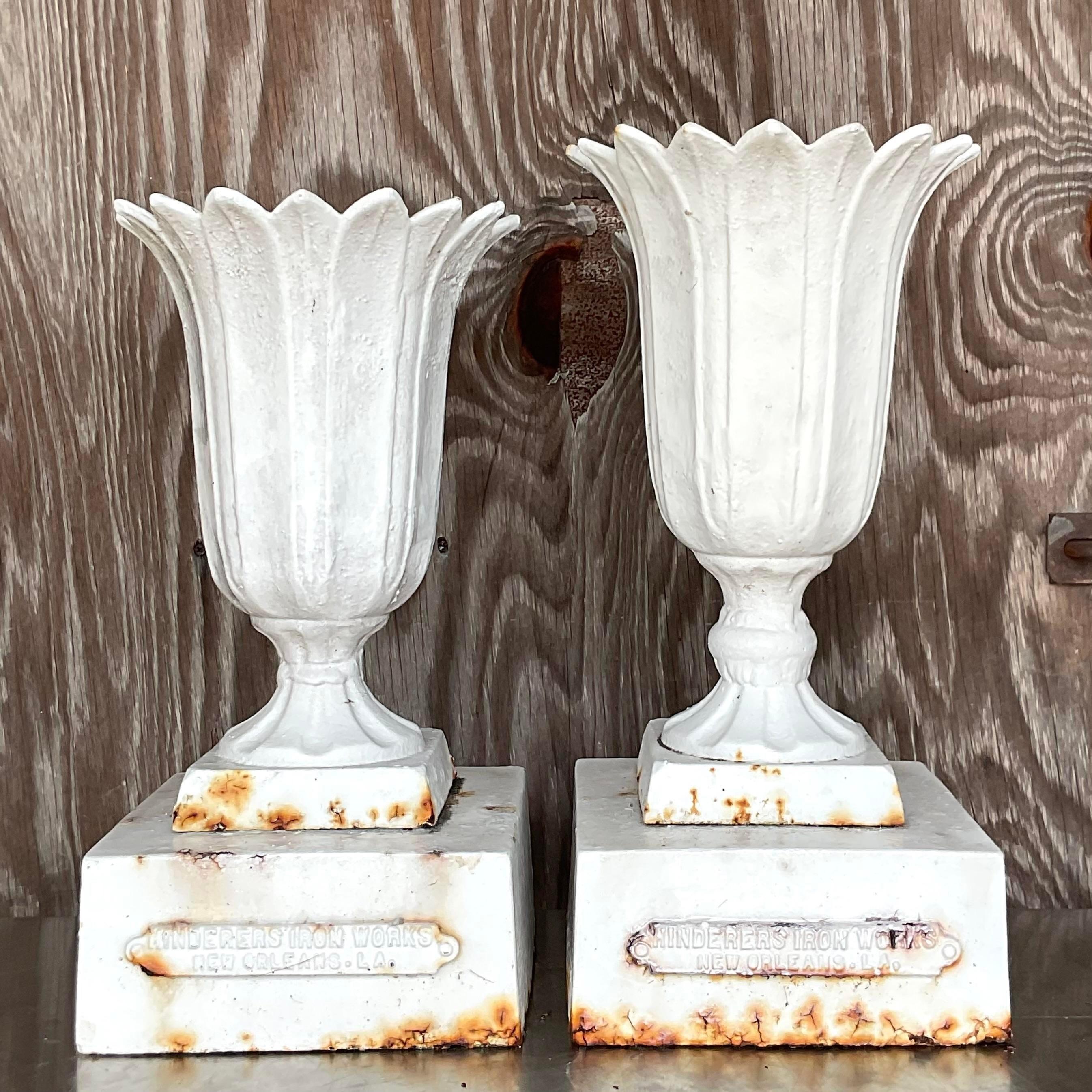 A fabulous set of two vintage urns. Made from a heavy case iron and painted white. An all over patinated rusty finish from time. Made by the Hinderson group in New Orleans and marked on each urn. Acquired from a Palm Beach estate.

Lower urn is
