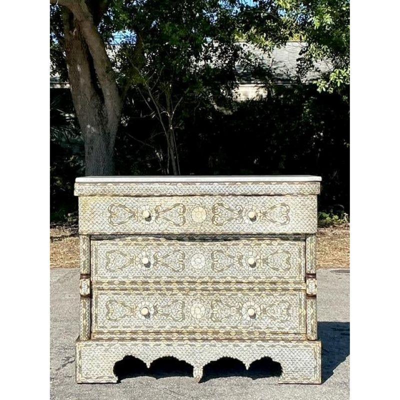 Eleva il tuo spazio con questa squisita cassettiera vintage a intarsio, impreziosita da intricati dettagli in osso o finto osso e coronata da un lussuoso piano in marmo bianco. Realizzato a mano con eccezionale maestria, il frontale a serpentina e i