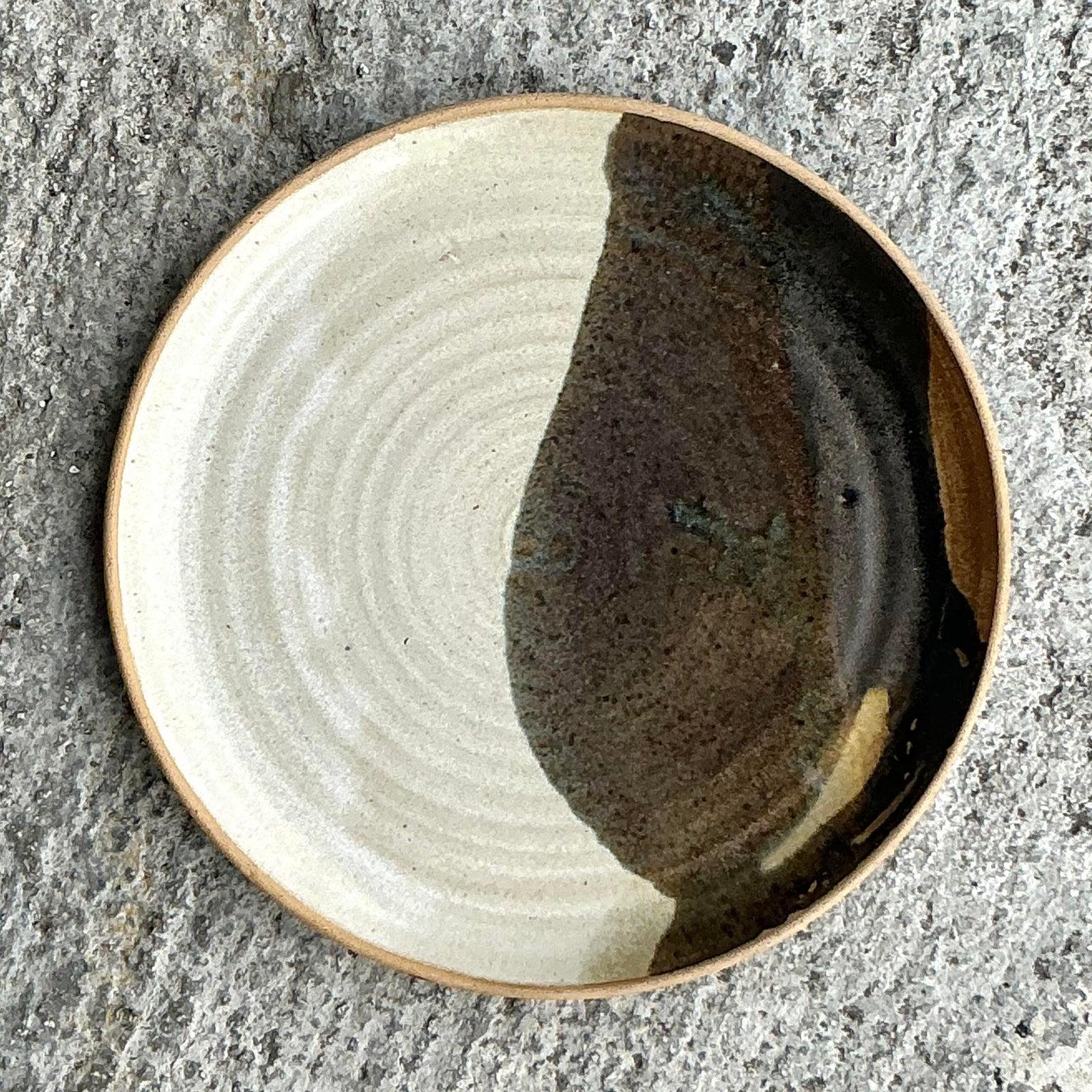 Scopri la singolare maestria dell'acclamata ceramista Jess Lord con questo squisito piatto vintage in Studio Pottery. Esempio magistrale di maestria artigianale, questo pezzo presenta uno smalto bicolore drammatico e ben eseguito: una metà di un