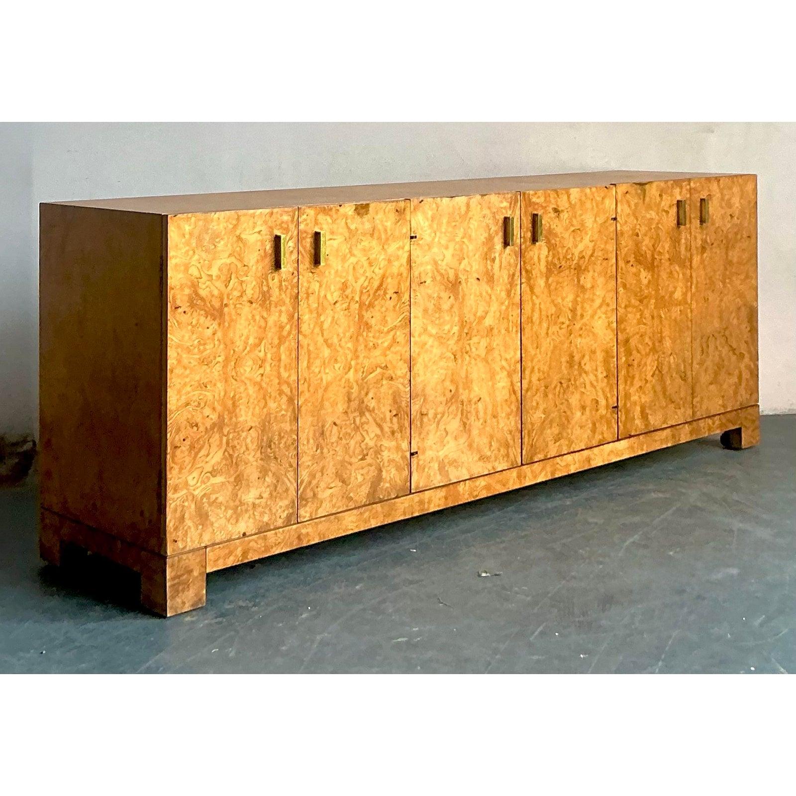 This exceptional long credenza is attributed to the esteemed John Widdicomb company, known for their high-quality, transitional furnishings of the mid-to-late 20th century. The piece is veneered in striking, highly figured burl wood, giving it
