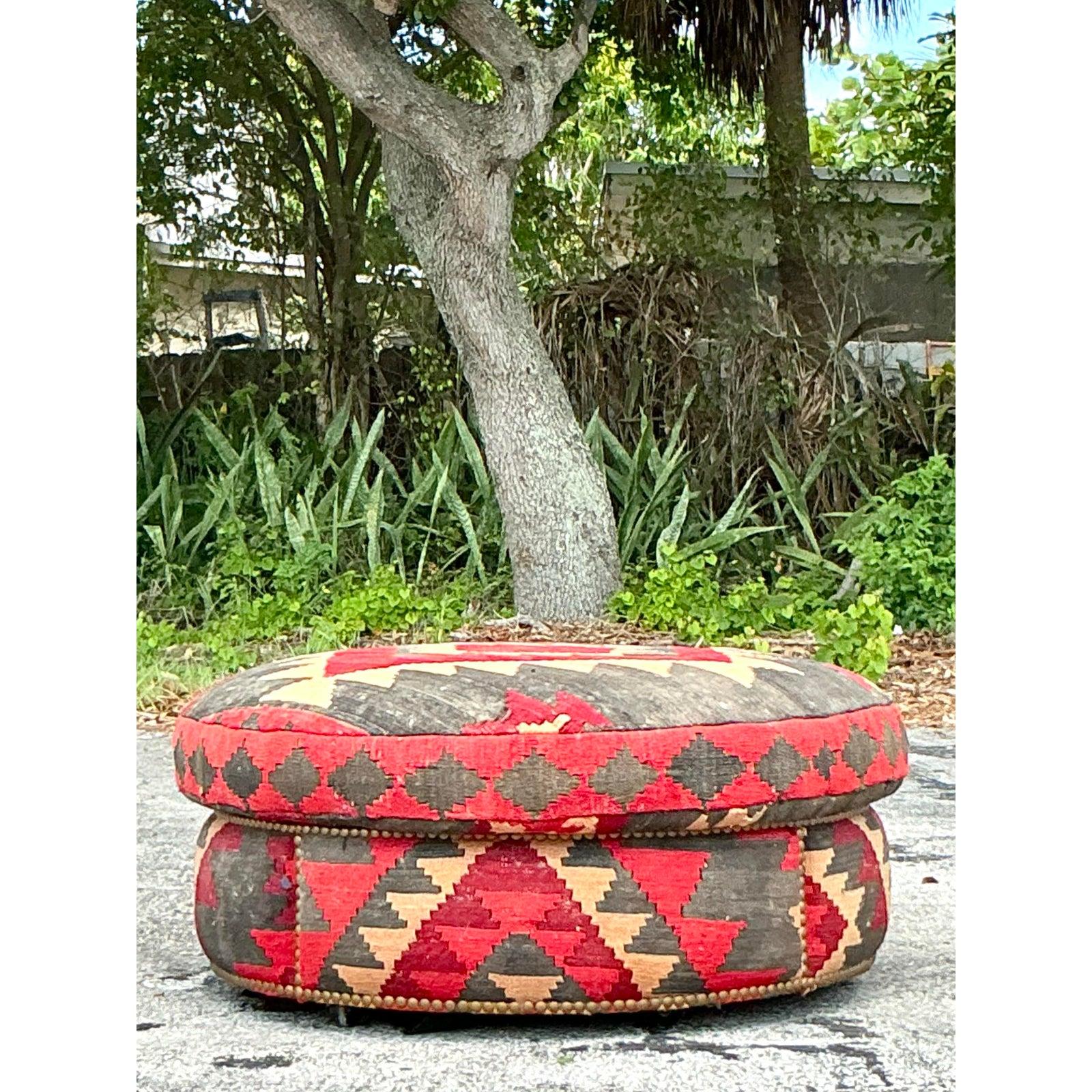 Ancrez votre espace de vie avec la texture riche et l'âme globale de ce superbe ottoman Kilim vintage ! Tapissé d'un authentique textile Kilim, il présente des motifs géométriques captivants dans des tons rouges, noirs et beiges. Sa forme ronde