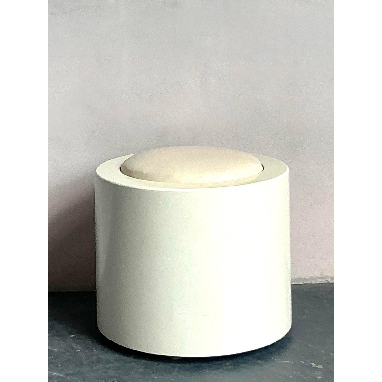 Eleva tu interior con este encantador taburete bajo vintage, una pieza encantadora que combina sin esfuerzo la sensibilidad boho chic con un toque de diseño minimalista. Fabricada con un acabado lacado en blanco impoluto, su forma cilíndrica y