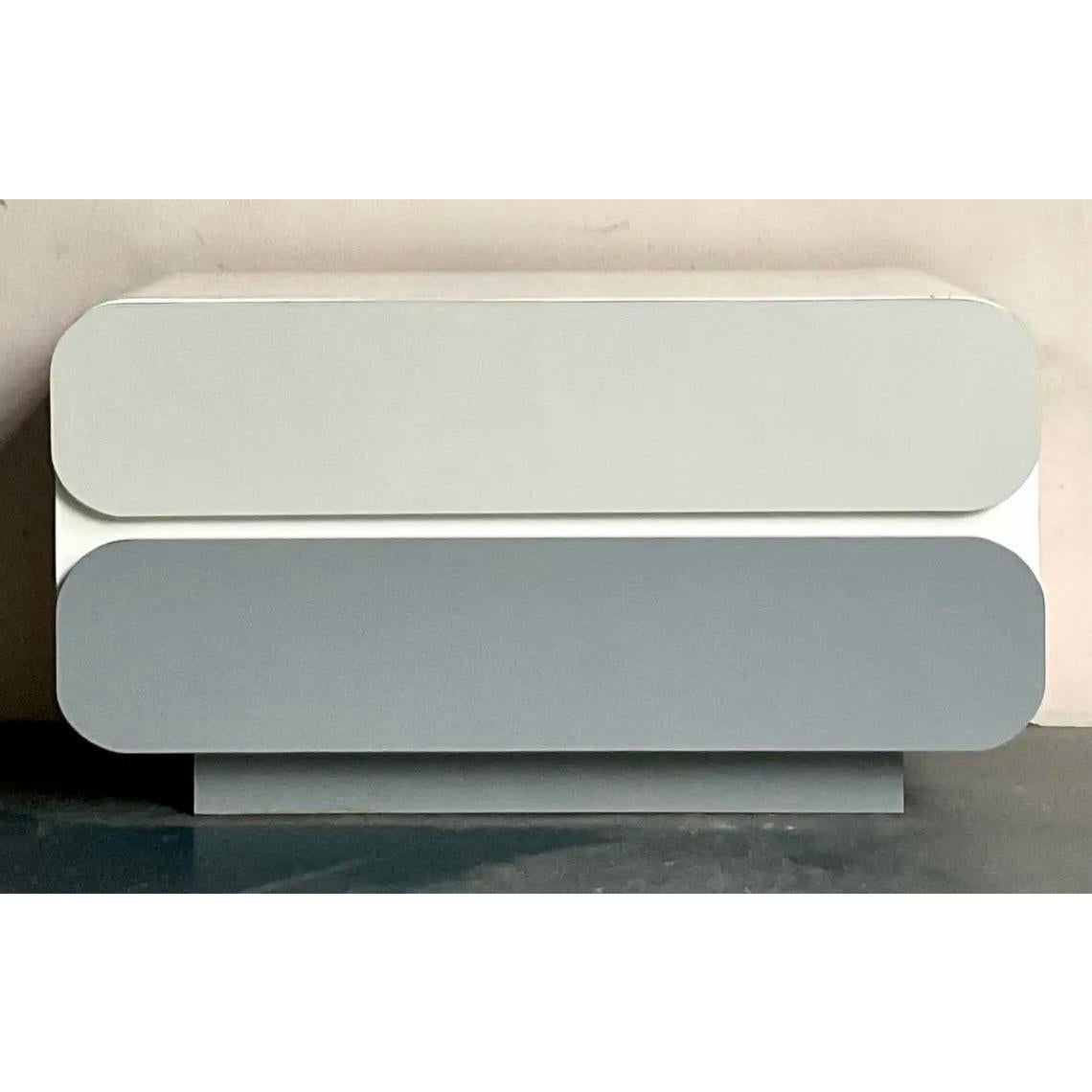 Adopta la estética distintiva de finales del siglo XX con esta cómoda laminada postmoderna vintage. Esta pieza irradia un encanto juguetón pero sofisticado, caracterizado por sus elegantes bordes redondeados y un cautivador acabado bicolor en gris