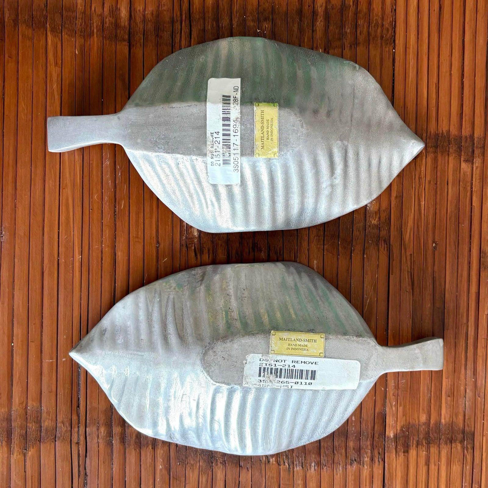 Maitland smith. These two sculptural dishes, shaped like stylized leaves, are crafted from a silvery metal with soft matte sheen and gently ribbed texture. Their flowing forms and curved edges mimic the natural contours of foliage, offering both