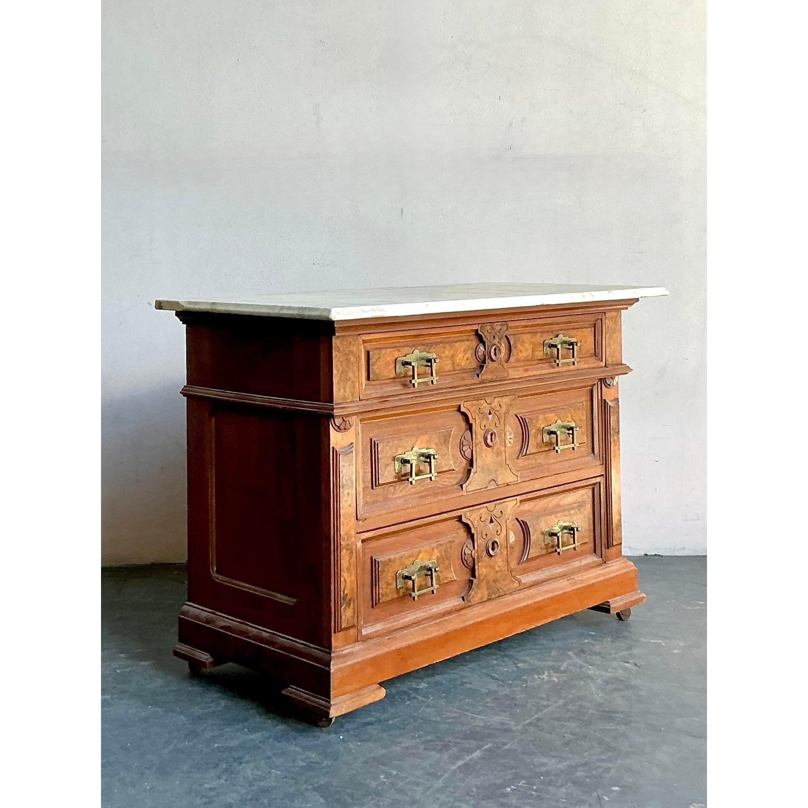 Cette exquise commode est une pièce de renaissance très détaillée, célébrant la richesse ornementale des périodes baroque ou rococo, interprétée pour un marché de luxe du milieu du XXe siècle. Le corps est revêtu d'un placage de loupe richement