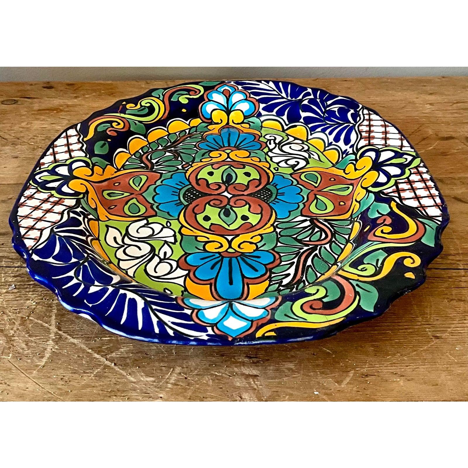Ce plat exubérant en céramique illustre la riche tradition de l'art populaire mexicain, rappelant le célèbre style Talavera avec sa palette vibrante et ses motifs floraux denses et stylisés. Le grès présente une étonnante palette de glaçures
