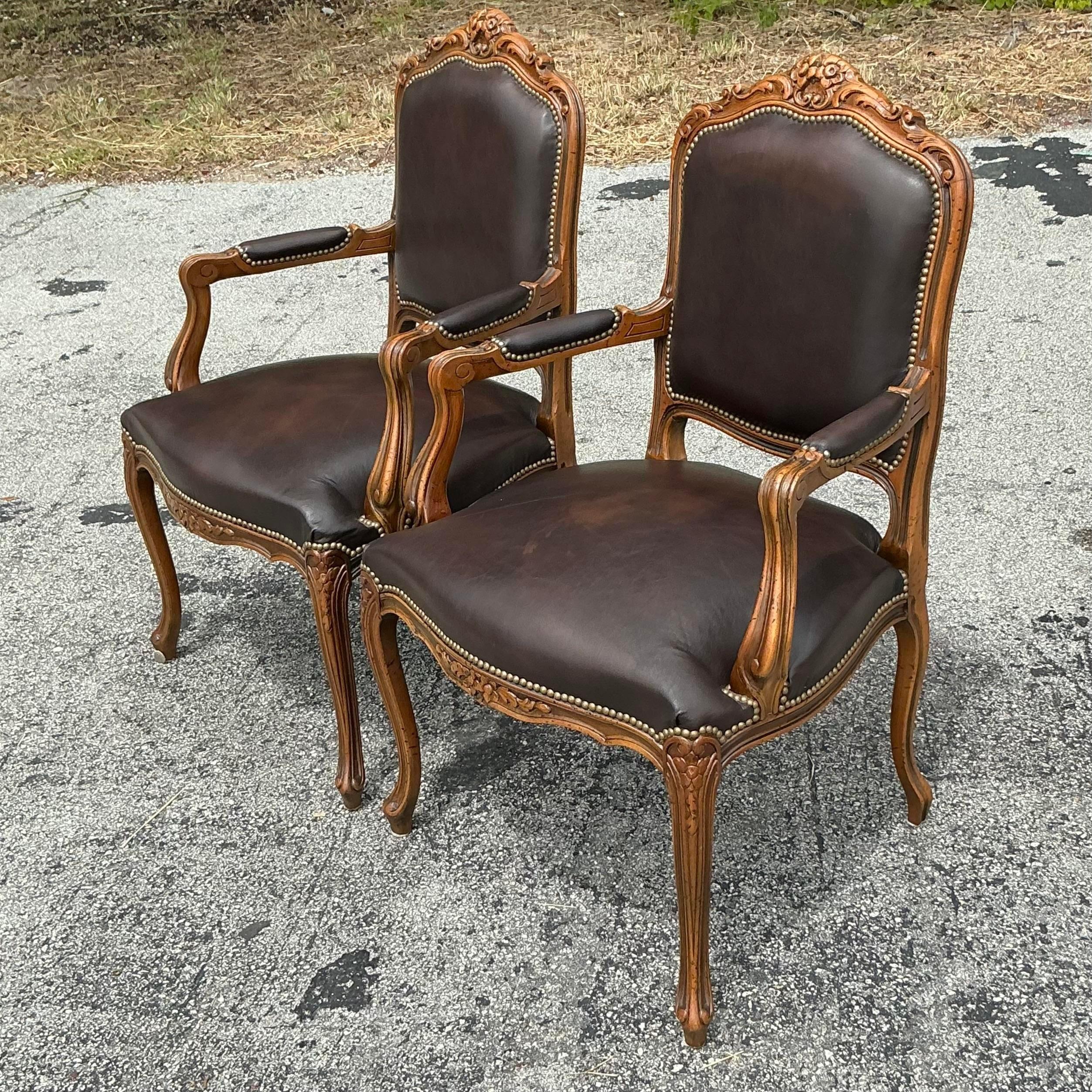 Eleva il tuo spazio con queste sedie Fauteuil in pelle Vintage Regency. Questa elegante coppia è caratterizzata da uno stile classico americano con un ricco rivestimento in pelle, cornici in legno intricatamente intagliate e una soffice imbottitura.