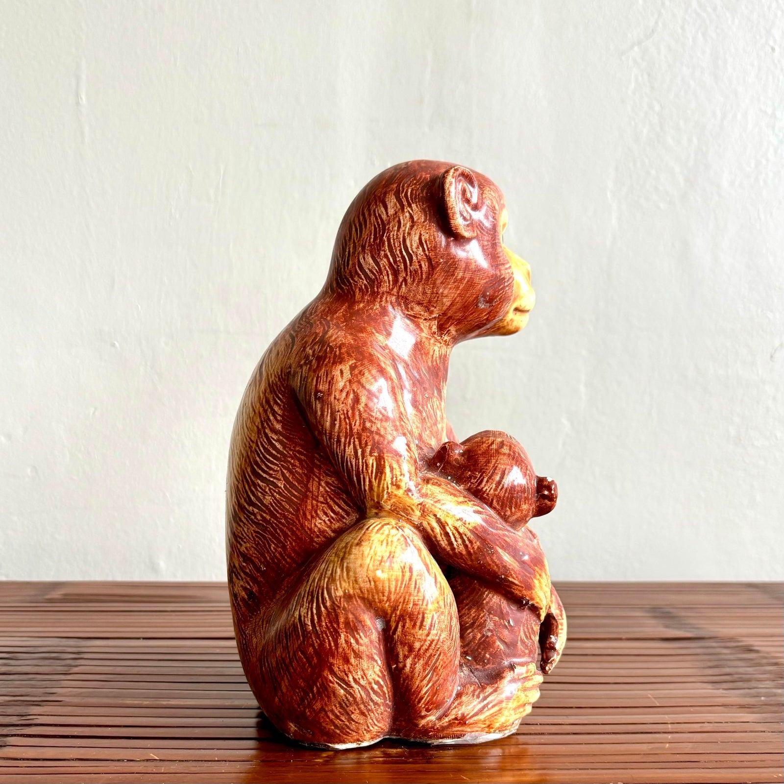 Questa scultura in ceramica cattura un tenero momento tra una madre scimmia e il suo piccolo, reso con dettagli espressivi e un caldo smalto marrone rossastro. Lo sguardo calmo e consapevole della madre contrasta delicatamente con lo sguardo curioso