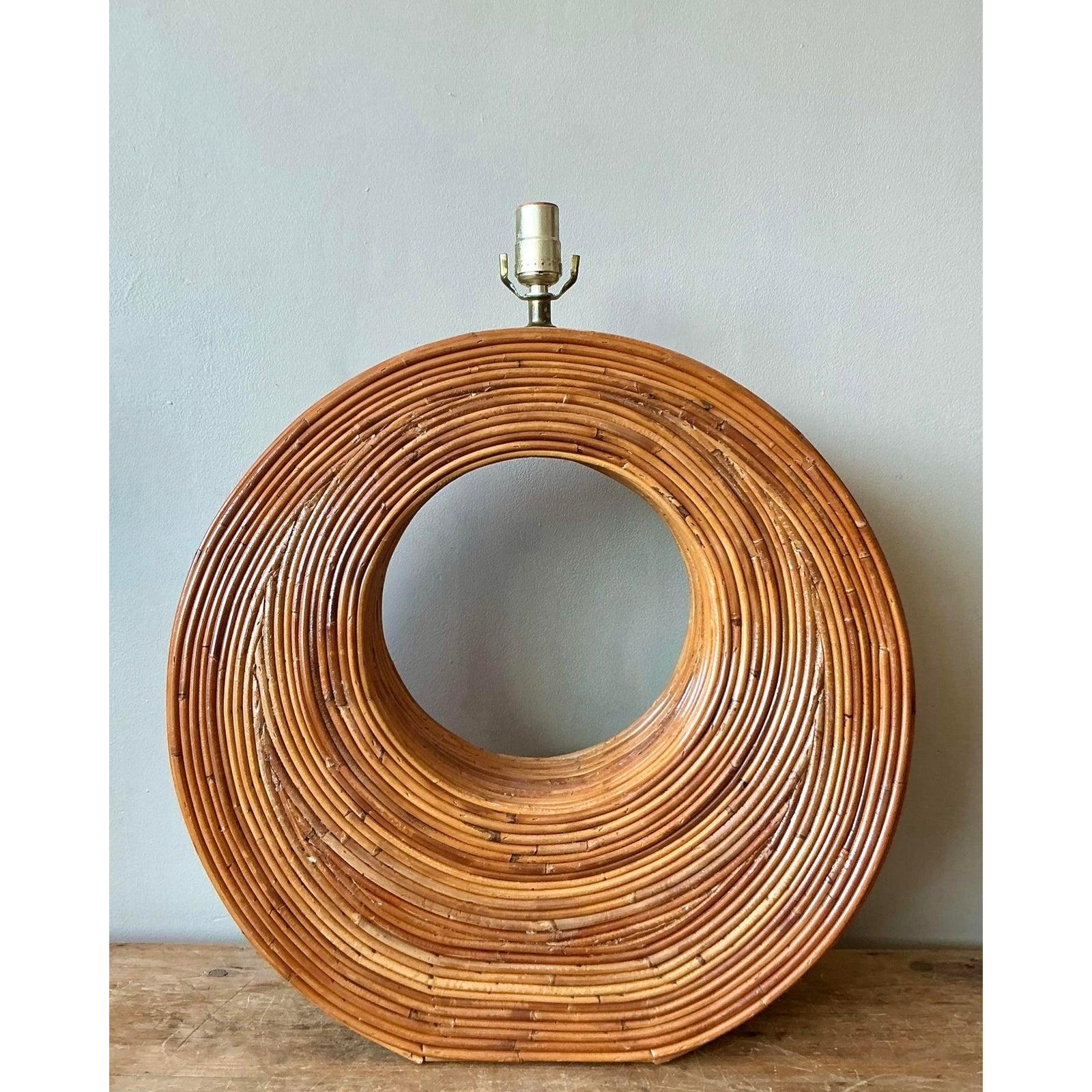 Make a spectacular sculptural statement with this monumental vintage pencil reed rattan table lamp. Designed with a bold, architectural presence, the lamp features a massive torus (doughnut) shape constructed from tightly coiled strands of natural