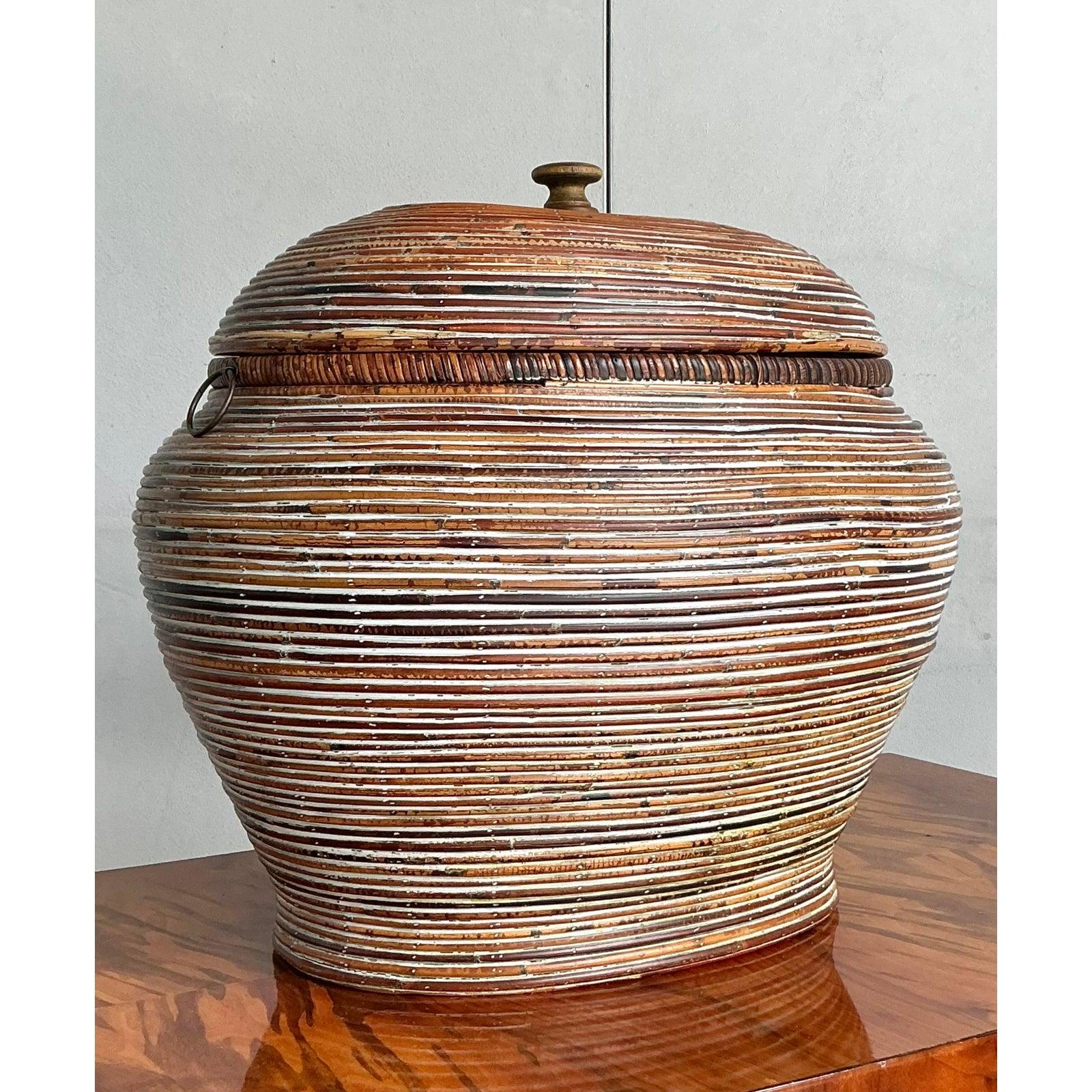 Questo magnifico cestino vintage con coperchio è una testimonianza di artigianato naturale e di eleganza bohémien. Realizzato in canna da zucchero meticolosamente intrecciata, presenta un sorprendente motivo a righe orizzontali ottenuto con diverse