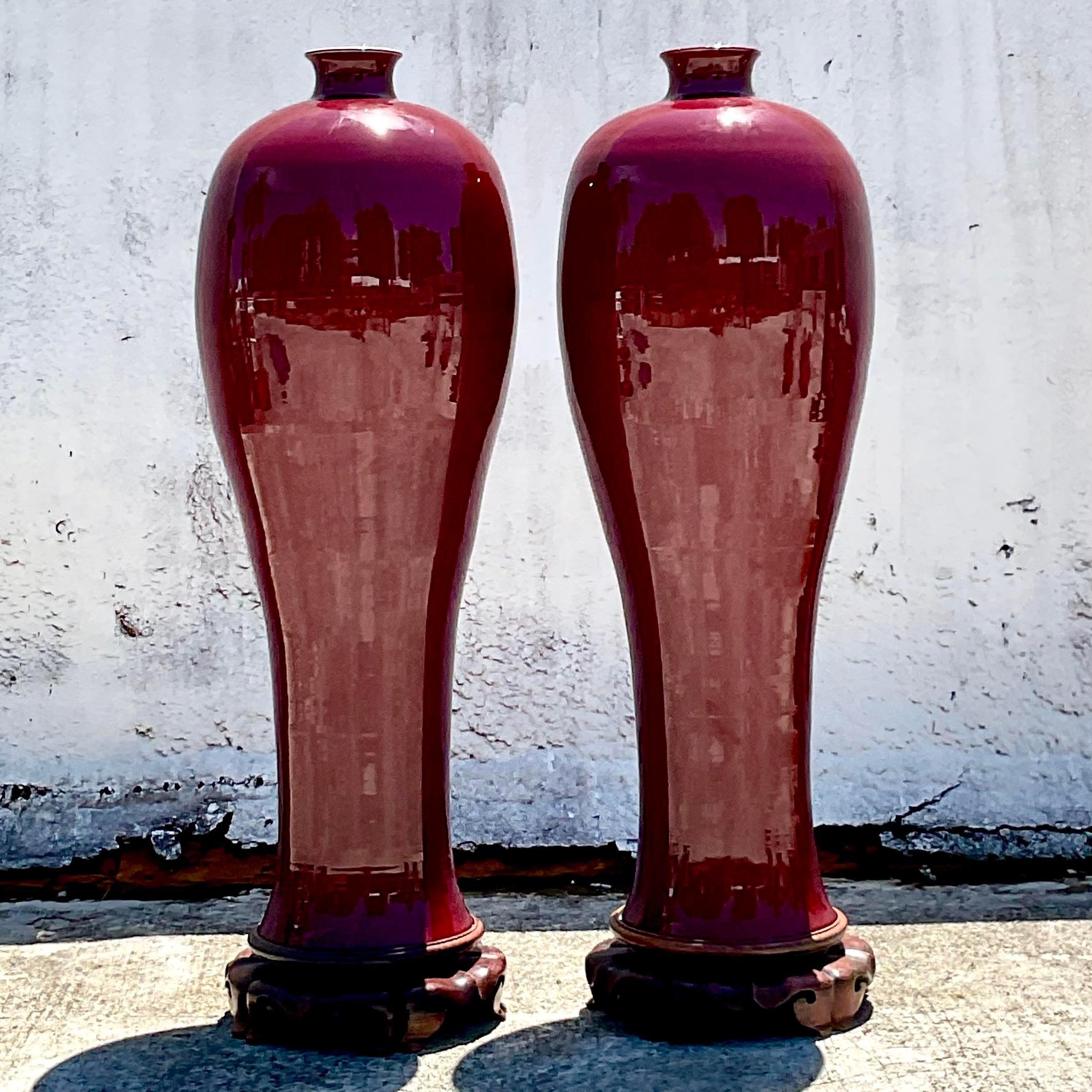 A fabulous pair of vintage Boho vases. A monumental pair in the “Sang de Bouf” style. Beautiful deep merlot color on Asian wooden pedestals. Acquired from a Palm Beach estate.