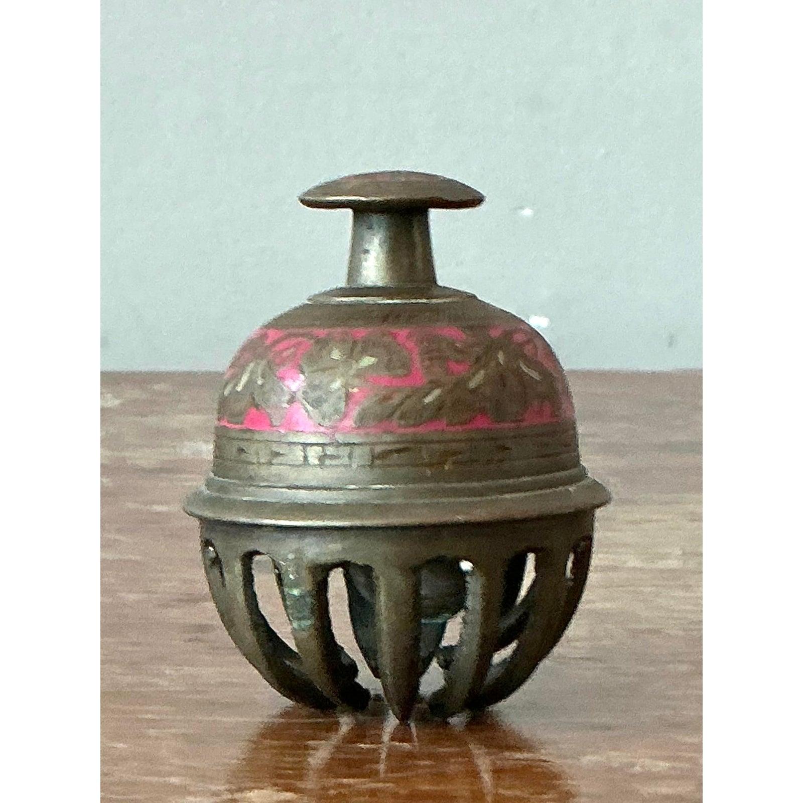 Infusez un charme exotique à votre intérieur avec cette délicieuse cloche marocaine vintage. Fabriquée en laiton vieilli, cette charmante pièce présente des détails gravés complexes et une touche vibrante d'émail rose, mettant en valeur les riches