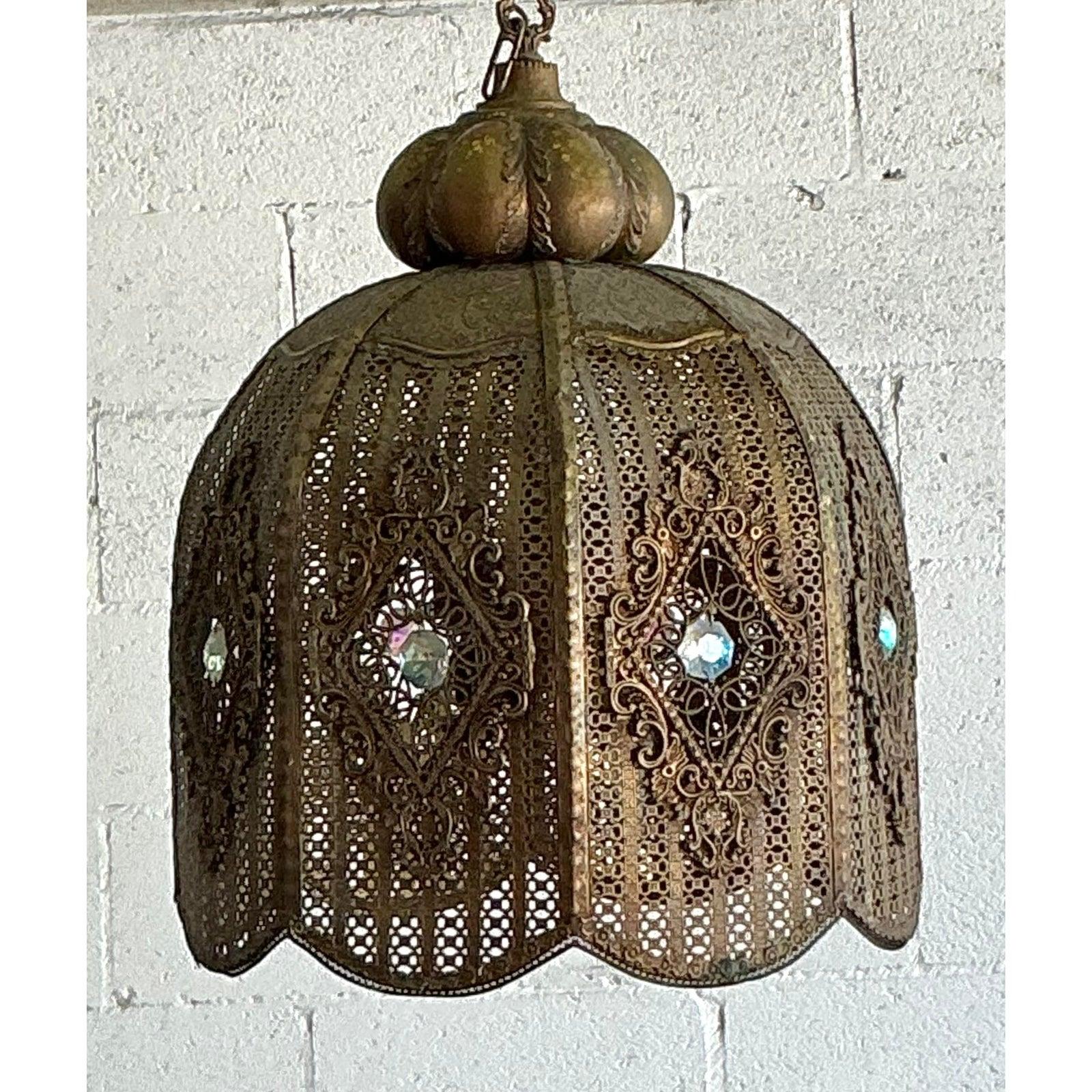Trasporta il tuo spazio in un bazar esotico e lontano con questa incantevole lanterna a sospensione in stile marocchino vintage. Realizzato meticolosamente a mano, questo grande ciondolo a cupola è caratterizzato da una filigrana di ottone