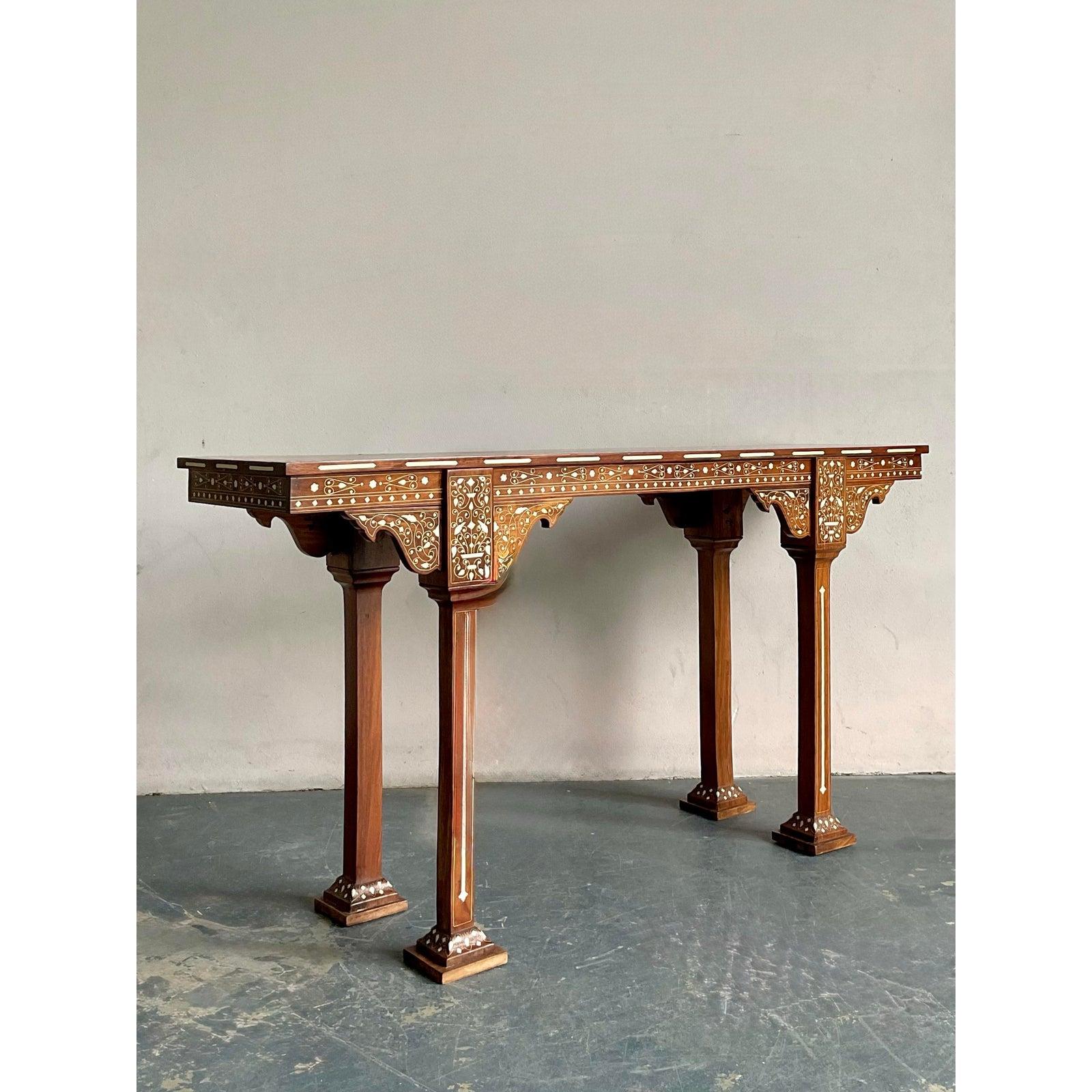 Imbue your entryway with the exotic allure and artisanal mastery of this magnificent vintage Syrian-style inlay console table. Handcrafted from rich, warm-toned hardwood, the table is meticulously embellished with intricate bone inlay in a
