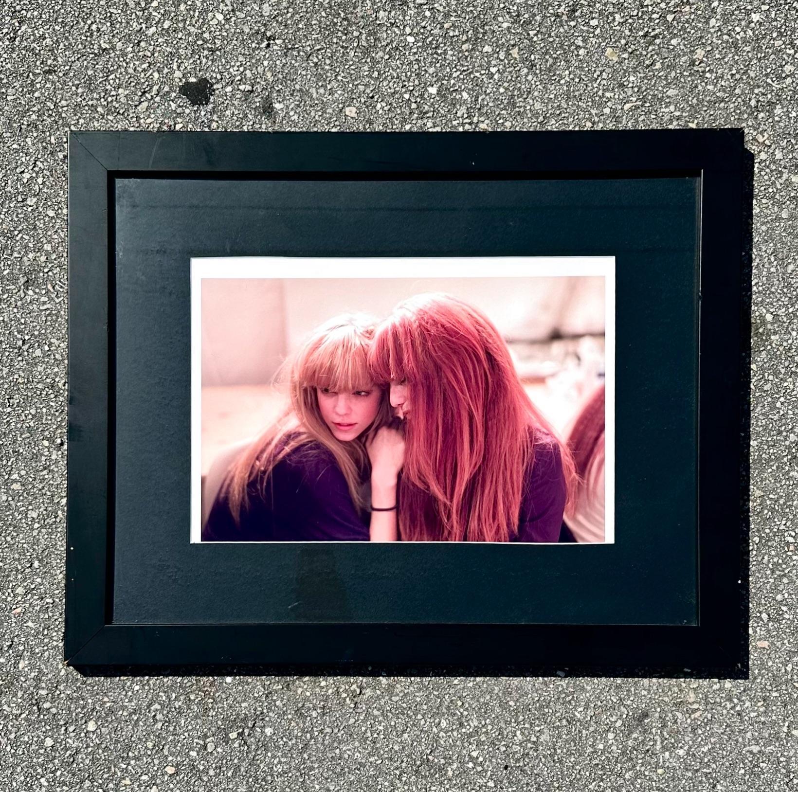This vintage photograph depicts 2 girls embracing each other enjoying the company of a friend. This stunning piece includes a black frame with contrasting red and sepia in the photo. Acquired from a Palm Beach estate. 