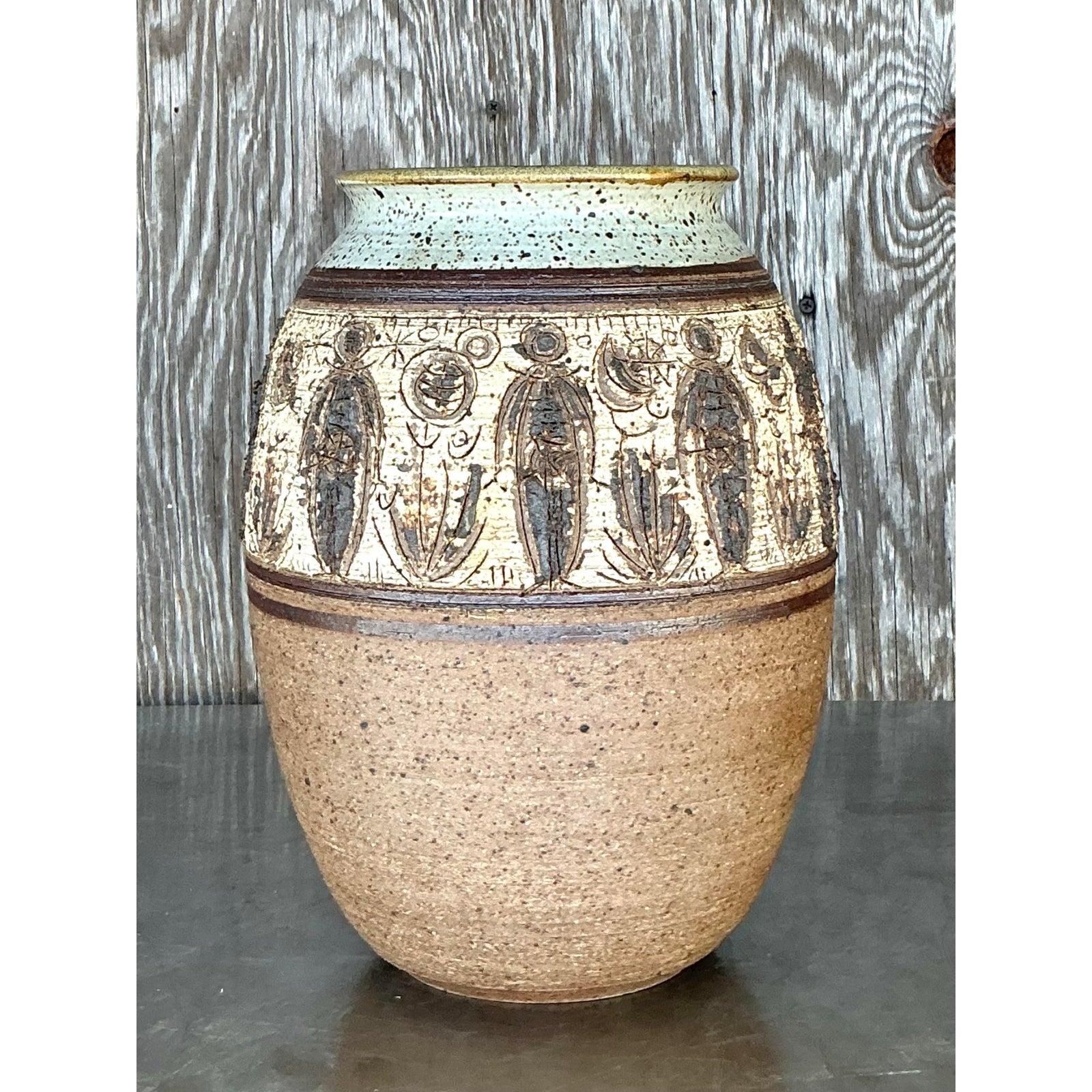 Questo squisito vaso vintage in Studio Pottery è una vera e propria opera d'arte, caratterizzata da un intricato disegno figurato intagliato a mano che incarna l'essenza dell'artigianato bohémien e di metà secolo. La base in ceramica grezza è