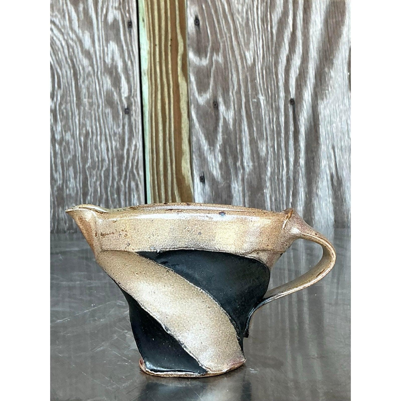 Add a touch of handcrafted artistry to your table or shelf with this distinctive vintage studio pottery pitcher. Its dynamic, sculptural form features a pleasingly organic shape with a gracefully integrated handle and a well-defined spout,