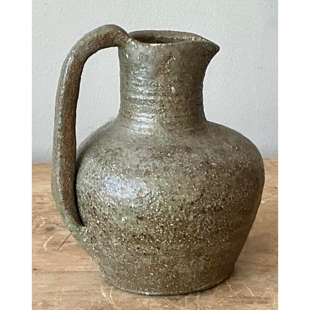 This raw and profoundly textural pitcher is a superb representation of mid-century Studio Pottery, celebrating the material's rustic authenticity. Hand-thrown, the vessel features an organically shaped body, an arched handle, and an uneven spout. It