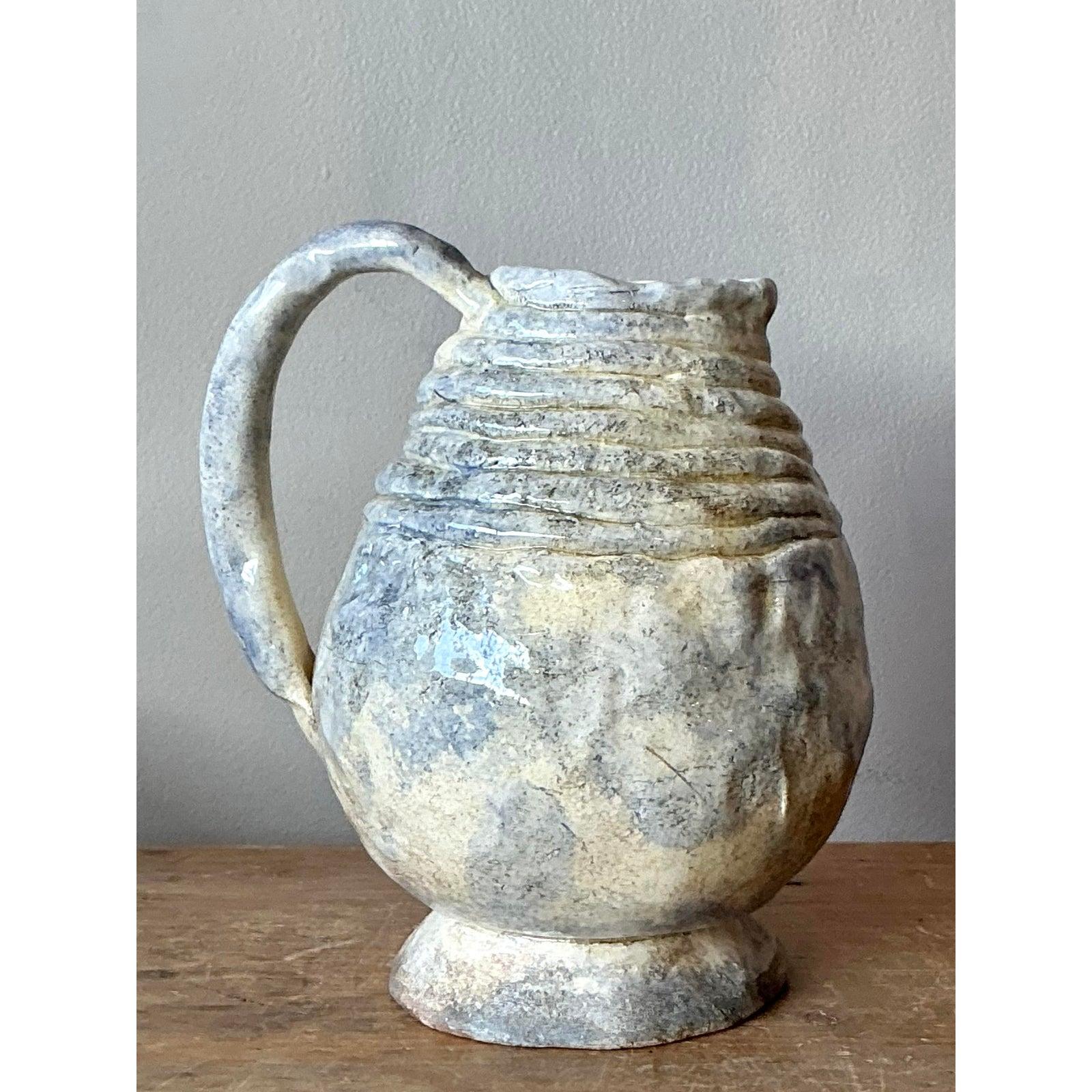 This unique vintage pitcher is an excellent example of mid-century studio art pottery, characterized by its hand-thrown, expressive form and rich, layered glaze. The body features pronounced horizontal rings and a subtly irregular silhouette, giving