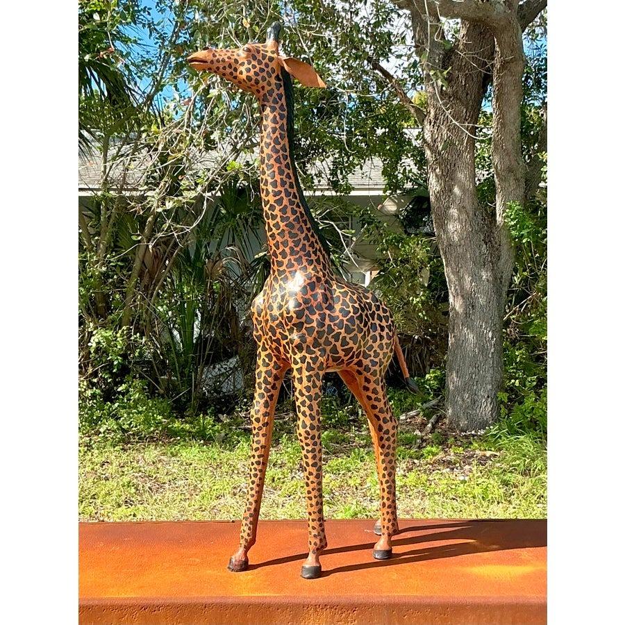 Aporta un toque de encanto exótico a tus interiores con esta escultura de jirafa de cuero pintado vintage. Hecha a mano con increíble atención al detalle, esta pieza luce un diseño rico y de tonos cálidos inspirado en los majestuosos dibujos de la