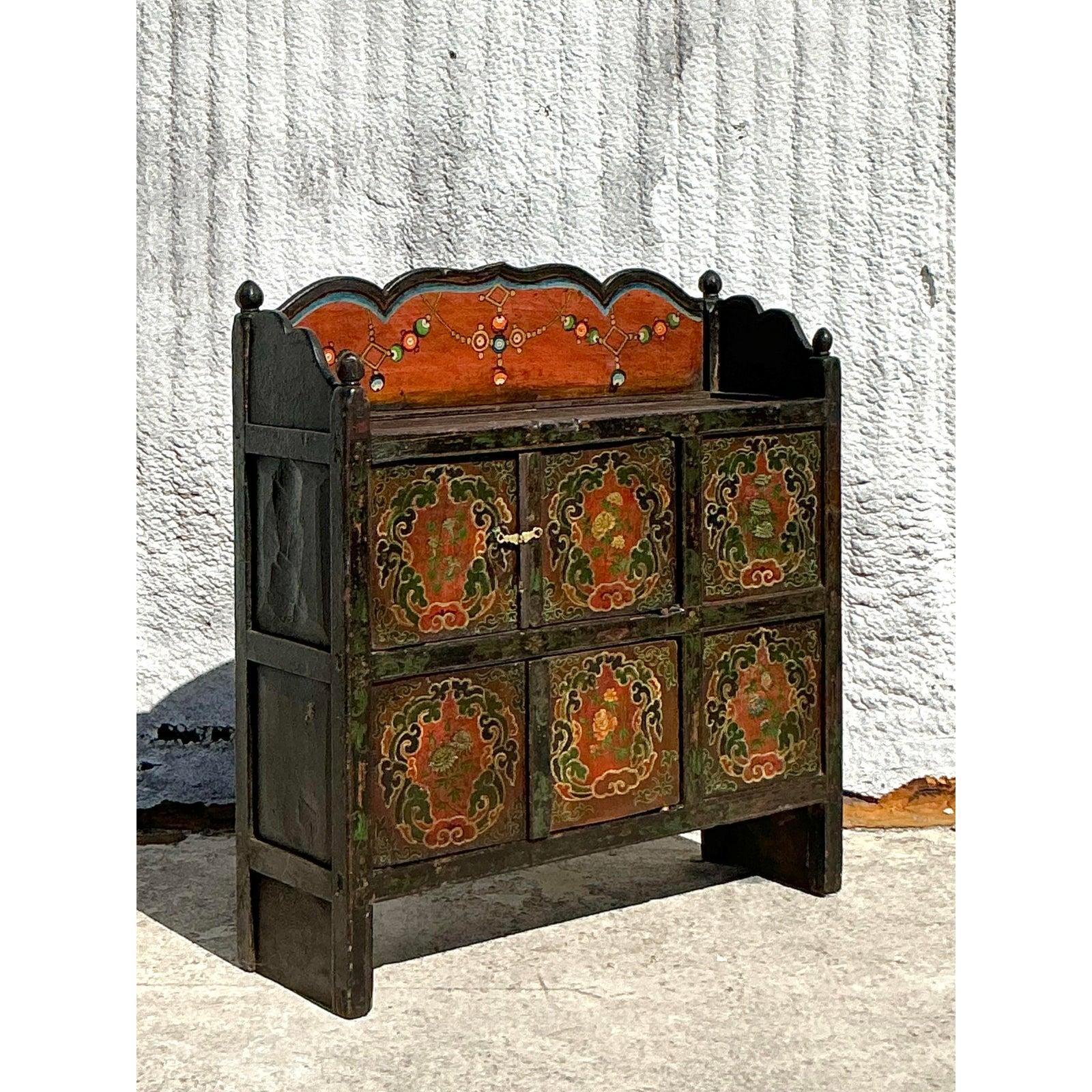 This exquisite vintage boho sideboard is a striking example of old-world craftsmanship, featuring hand-painted floral motifs in deep, rich tones of green, red, and gold. The distressed finish and ornate detailing reflect a well-loved history,