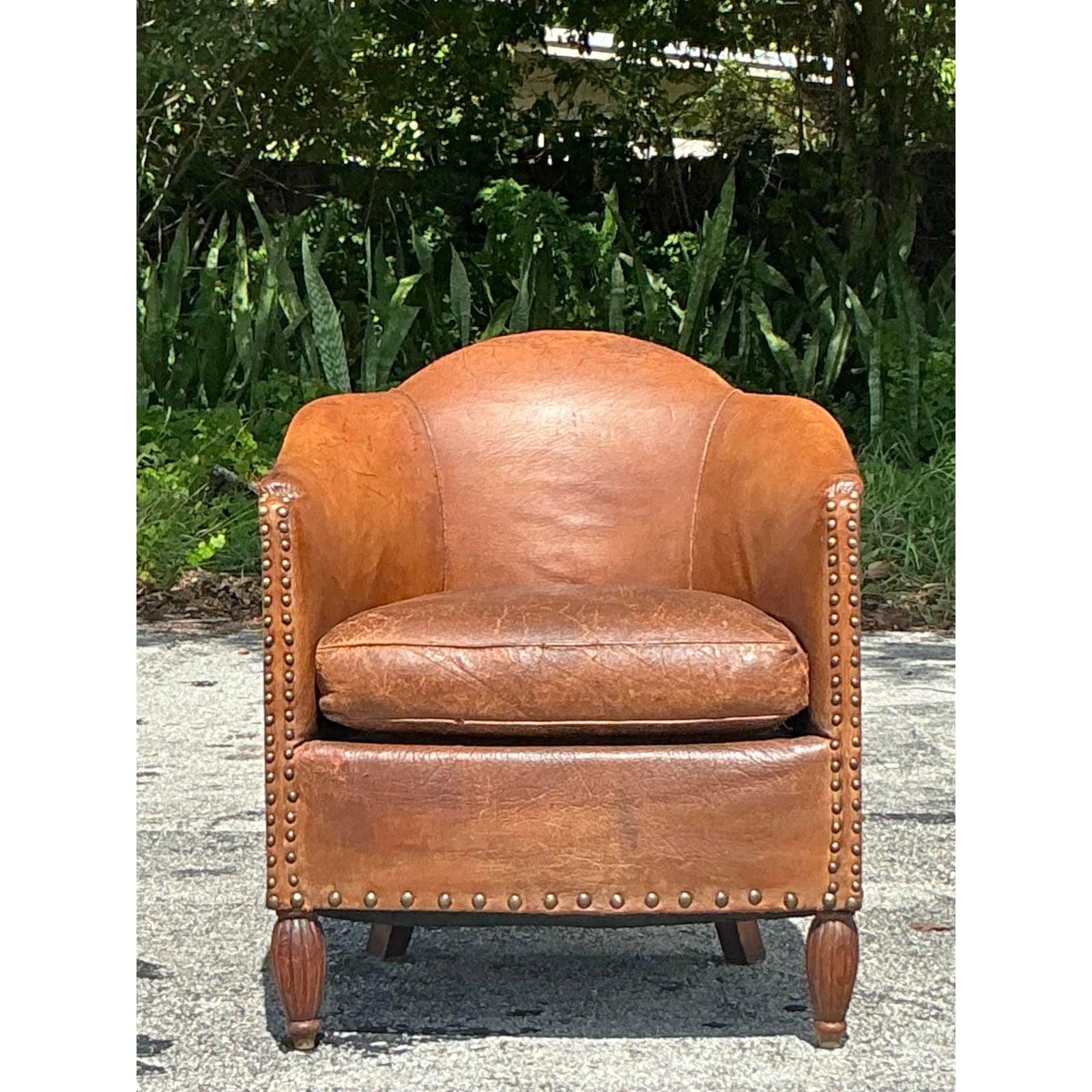 Sink into the timeless comfort and sophisticated charm of this exquisite vintage leather club chair. Embodying the classic elegance of a 1940s Parisian salon, this piece features an iconic, enveloping barrel-back silhouette, crafted from buttery,