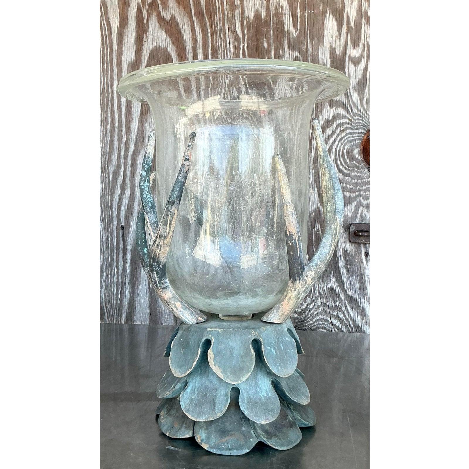 Introduci una miscela sorprendente di fascino rustico e stile bohémien con questo vaso a uragano vintage unico nel suo genere. Realizzato con un'abilità artistica irresistibile, è caratterizzato da supporti in stile corno che cullano un recipiente