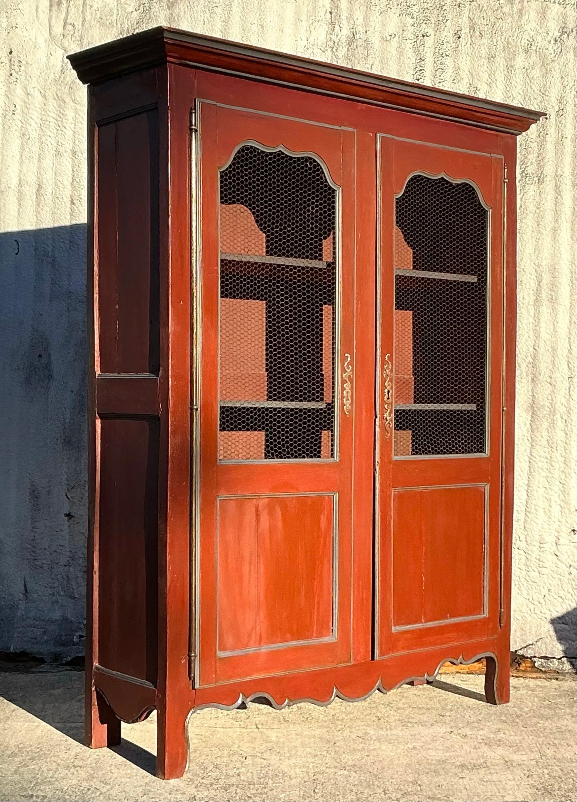 A stunning vintage boho armoire featuring a patinated finish and intricate wire front doors, exuding character and rustic charm. This piece offers ample storage with spacious shelving inside, making it both functional and stylish. The wire front
