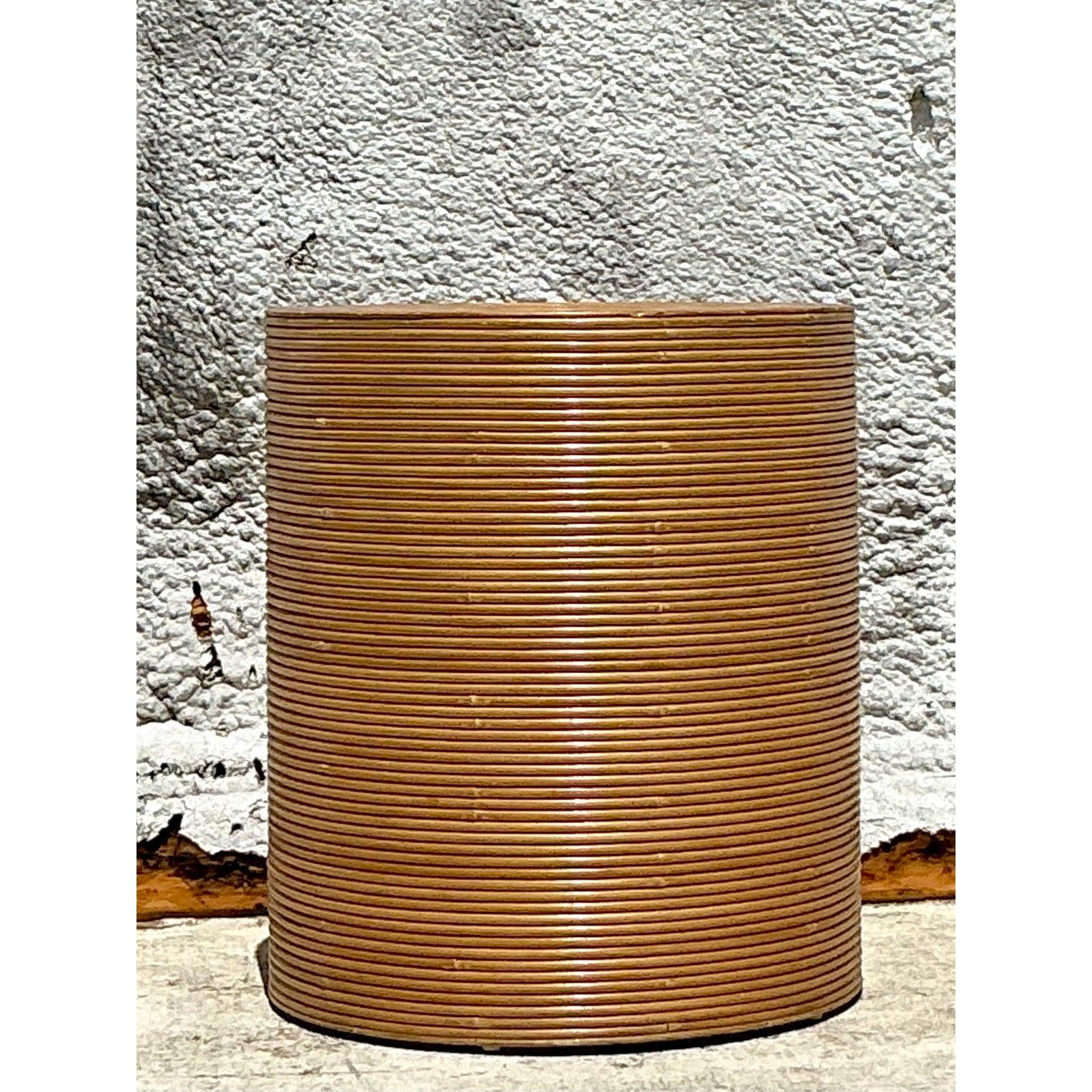 Embrace the chic, textural allure of 1970s design with this stunning vintage pencil reed table pedestal. Meticulously handcrafted by wrapping slender reeds of rattan around a solid cylindrical form, this piece showcases a sophisticated, hypnotic
