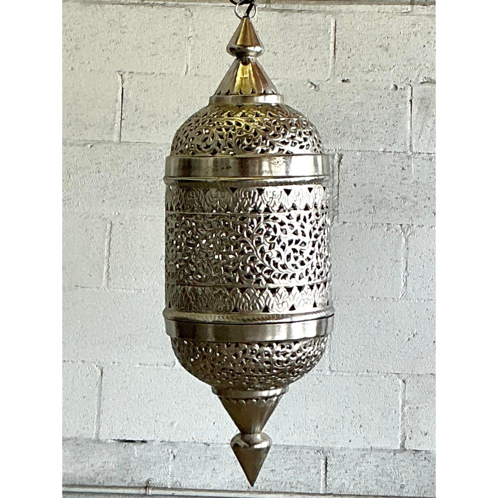 Infondi nella tua casa il fascino esotico di questa splendida lanterna marocchina vintage. Realizzato a mano in metallo argentato, l'intero corpo è meticolosamente traforato e cesellato con intricati motivi floreali e di vite, a testimonianza della