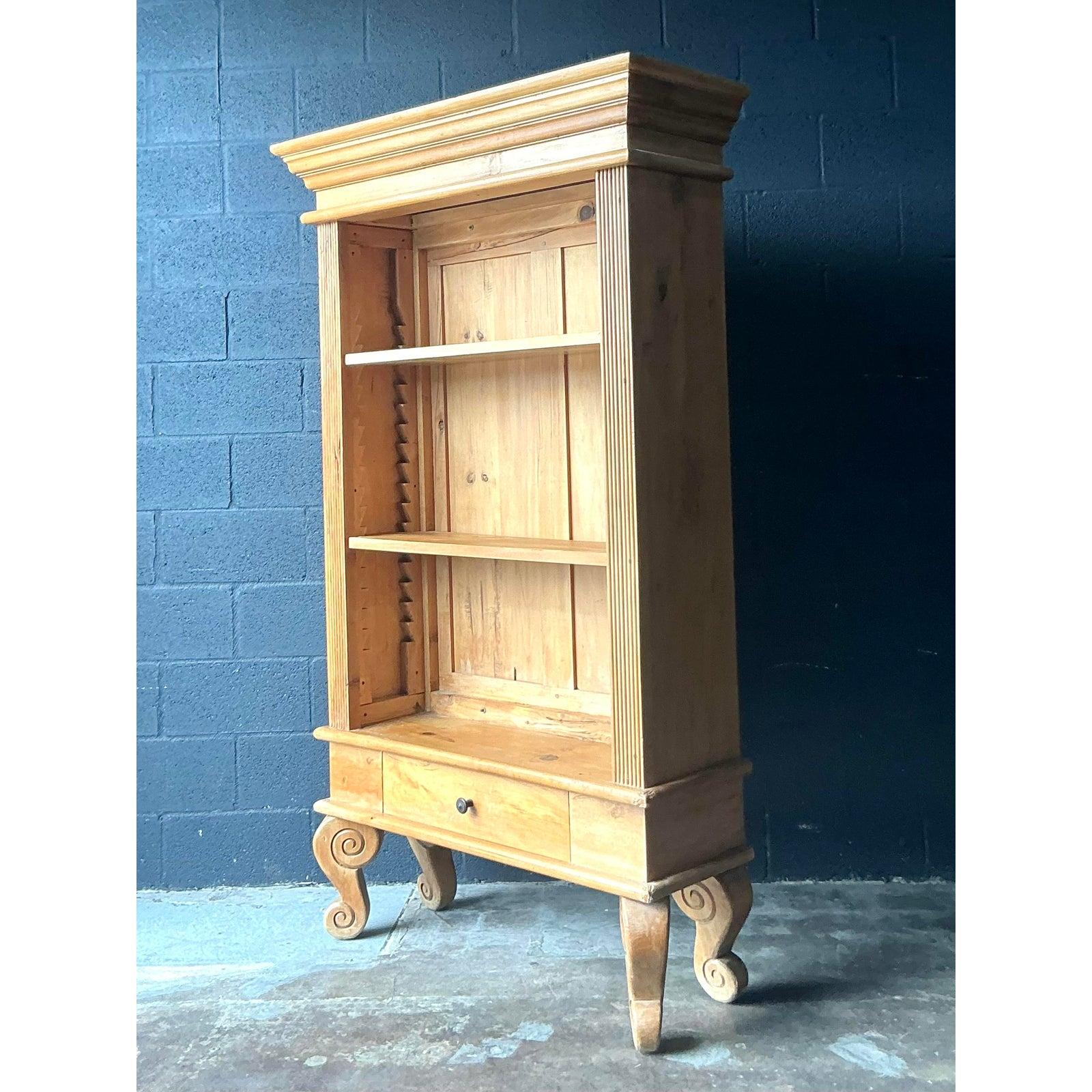 Cette imposante étagère ou vitrine offre un mélange sophistiqué de détails architecturaux traditionnels et de matériaux rustiques. Construite en pin brut ou légèrement teinté, la pièce présente des éléments néoclassiques tels qu'une importante