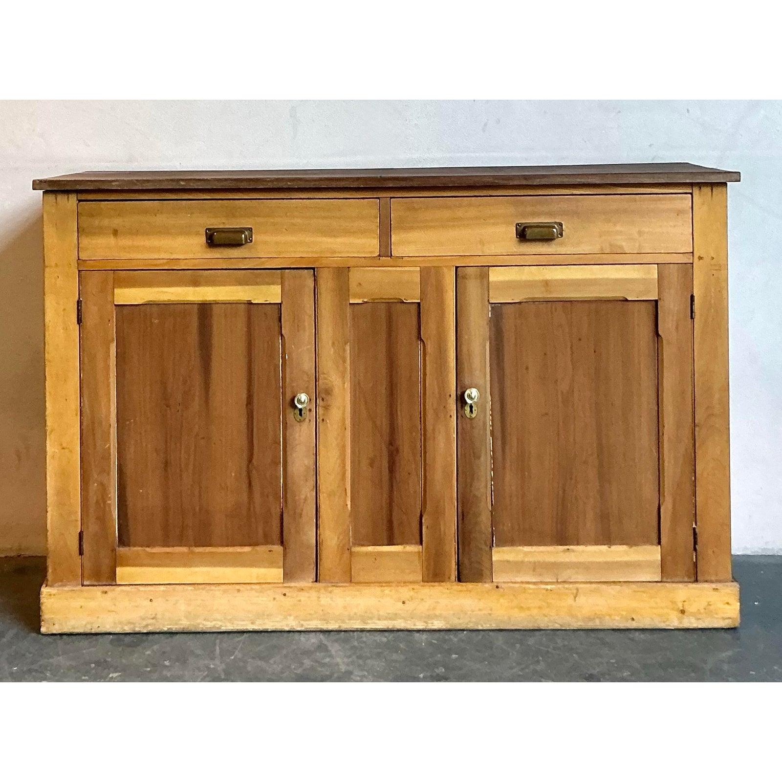Discover the charming allure of this vintage Boho Chic pine sideboard, a rustic and functional piece dating from the early 20th century. Crafted from warm, natural pine, this cabinet exudes an inviting, earthy aesthetic with its visible wood grain