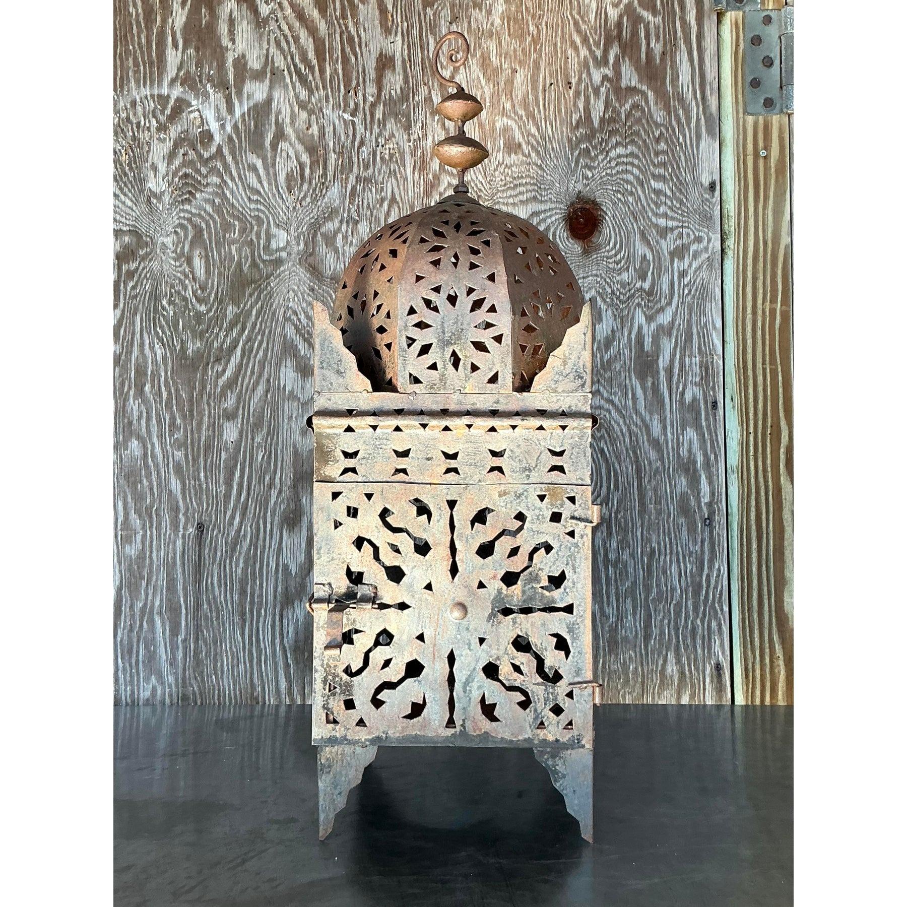 Aggiungi un tocco di fascino rustico e bohémien alla tua casa con questa squisita lanterna vintage in metallo tagliato a punzone. Caratterizzata da intricati motivi geometrici e da una sommità a cupola ornata da terminali decorativi, questa lanterna