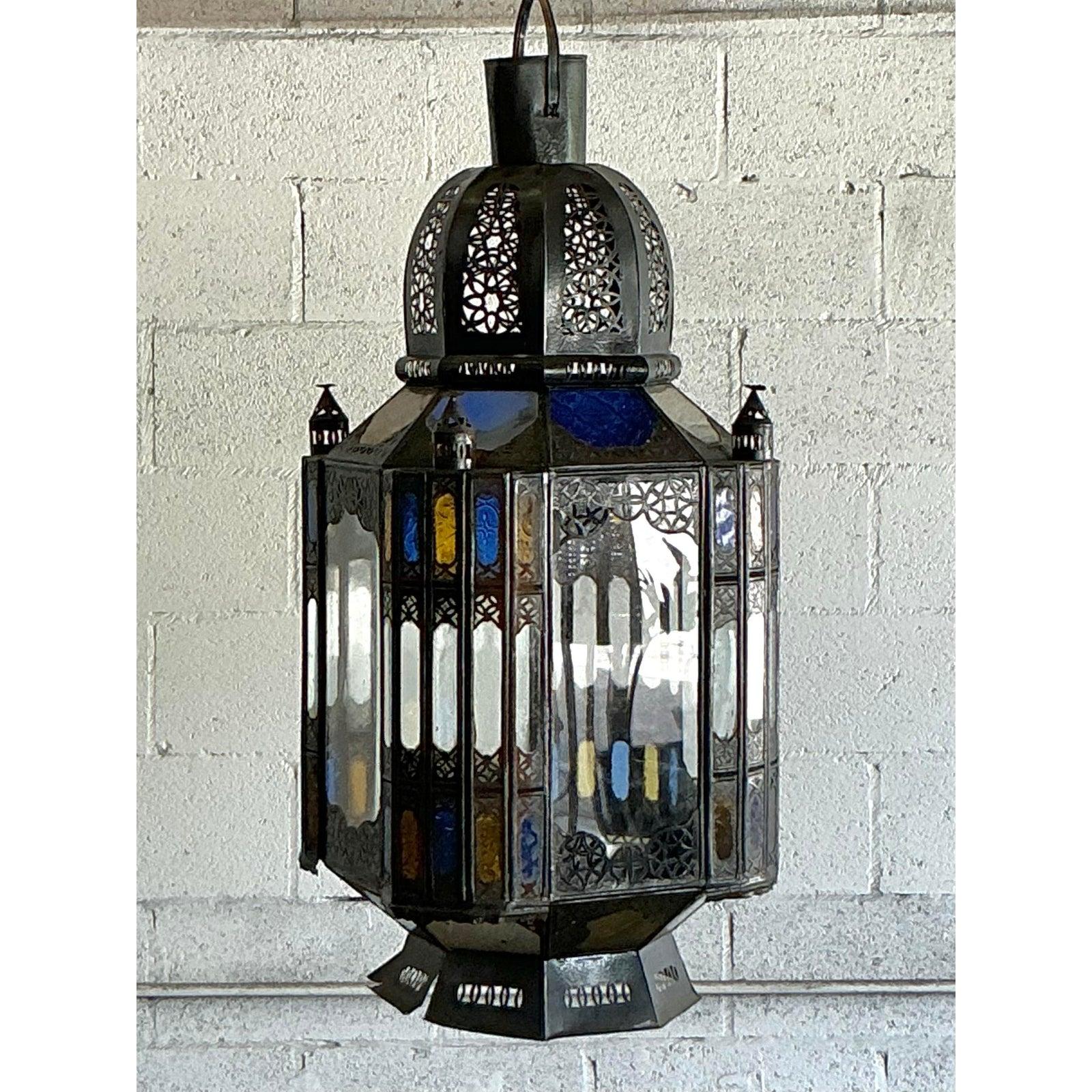 Trasporta il tuo spazio in un bazar esotico con questa incantevole lanterna marocchina vintage, una vera e propria testimonianza di artigianalità. Il suo design accattivante è caratterizzato da una ricca struttura in metallo dai toni scuri,