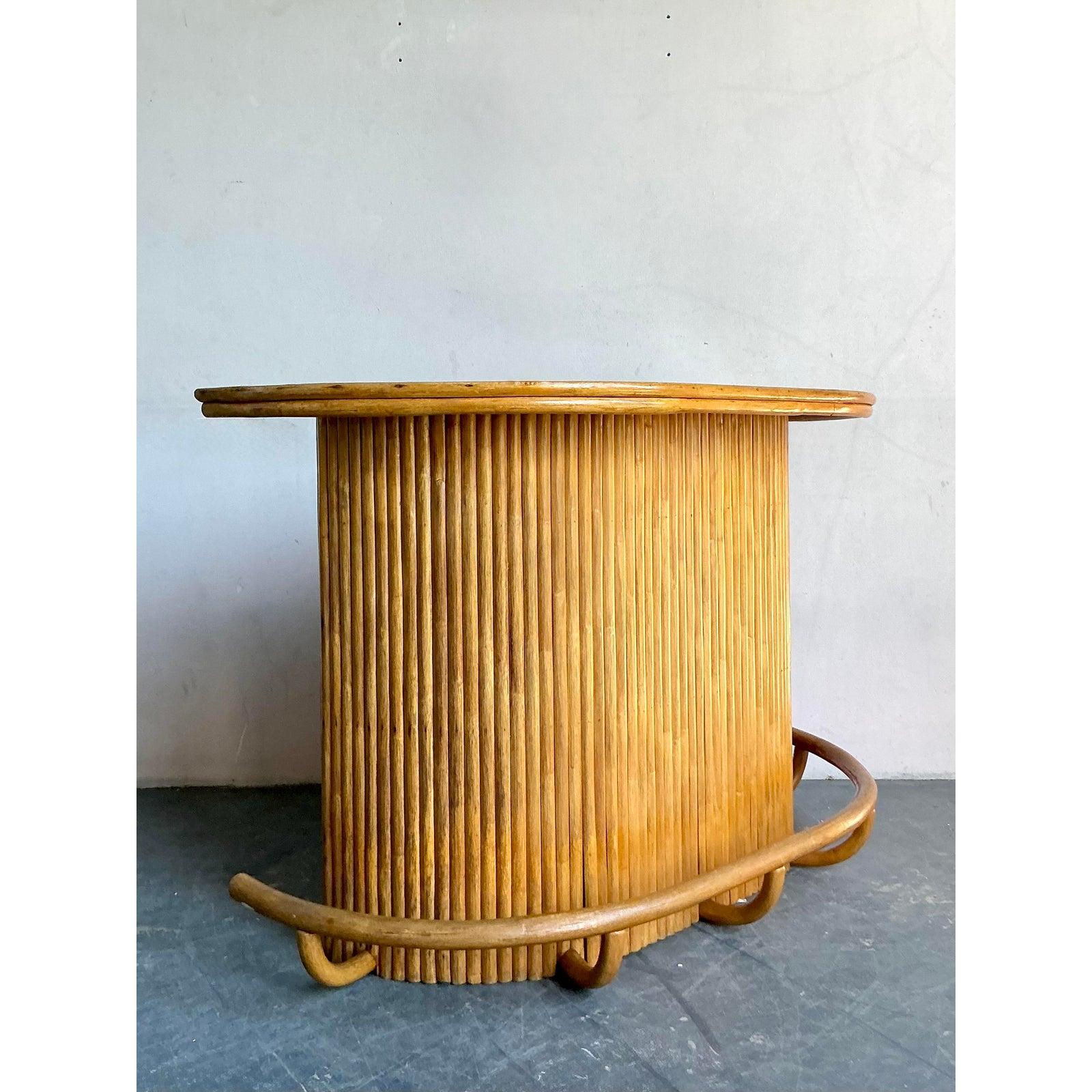 Infunde a tu espacio de entretenimiento el lujo relajado de este bar seco vintage de ratán y junco. Esta impresionante pieza se define por su escultural silueta en forma de riñón y su revestimiento vertical de caña partida, que ofrece una textura