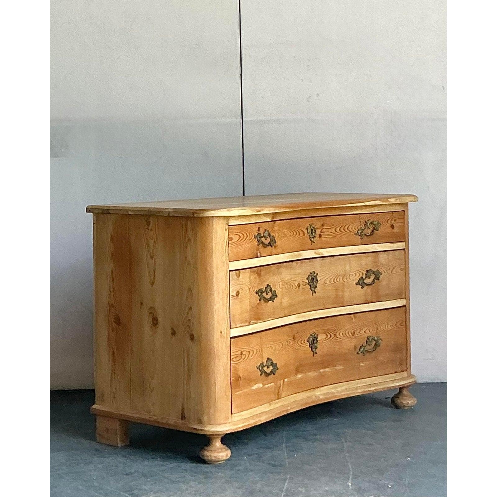 Exuding timeless European charm, this antique commode is a beautiful example of Biedermeier-style craftsmanship. Constructed from warm, knotty pine, the chest showcases the natural beauty of the wood grain, enhanced by a rich, aged patina. Its